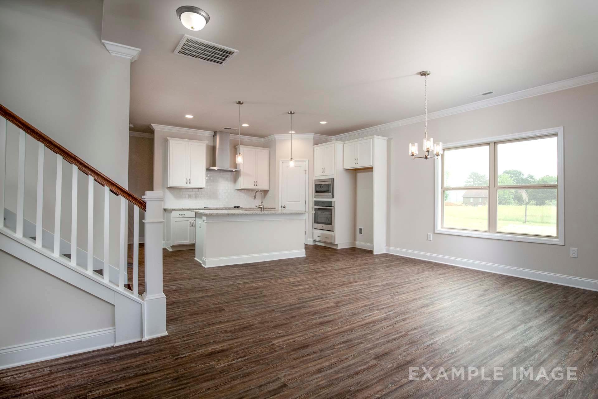 Open-concept kitchen in The Charleston Davidson Homes design featuring white cabinetry, large island, stainless appliances, hardwood floors, and staircase