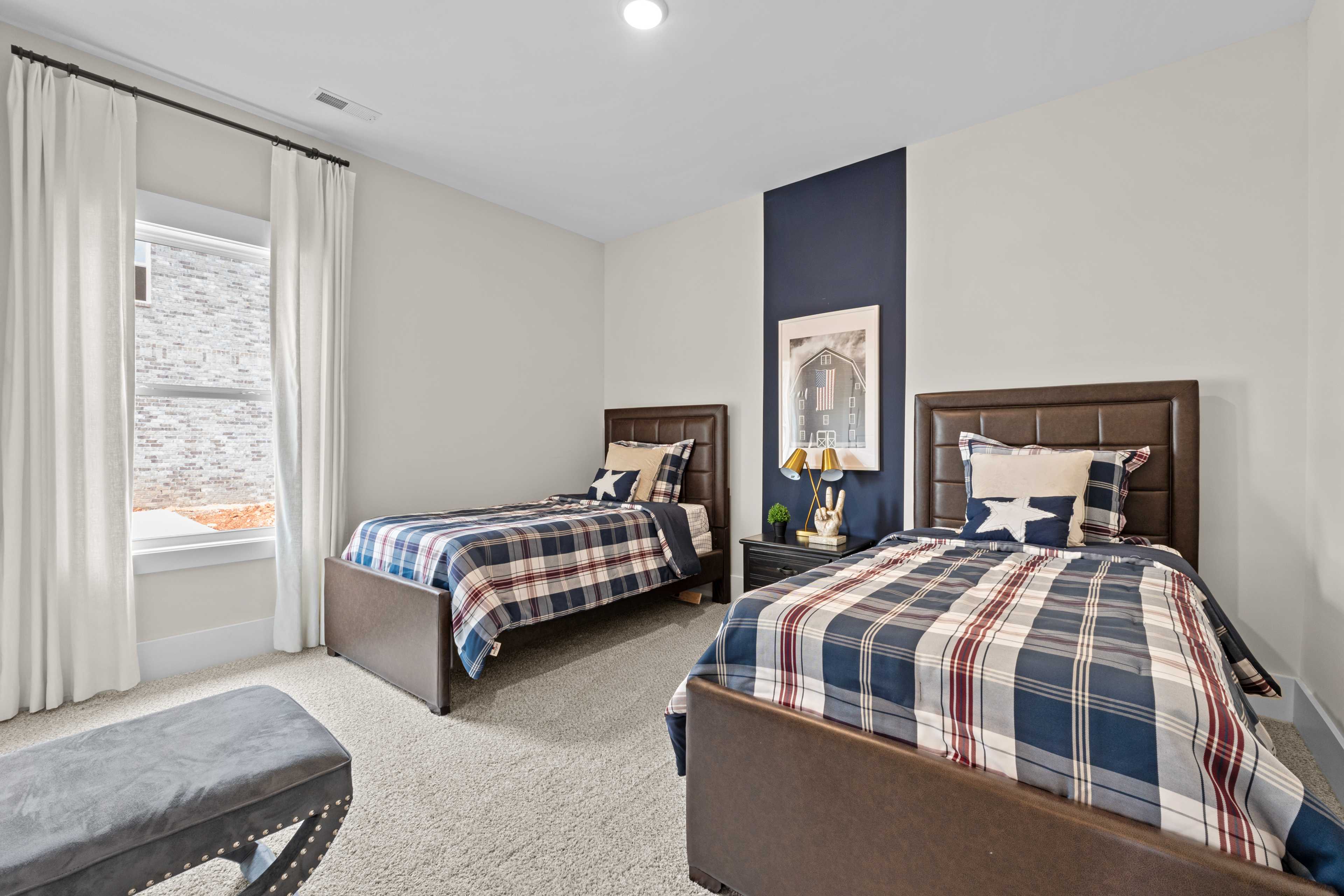 Cozy twin bedroom with navy accent wall, plaid bedding, and window drapes at Ivy Hills in Toney, Alabama