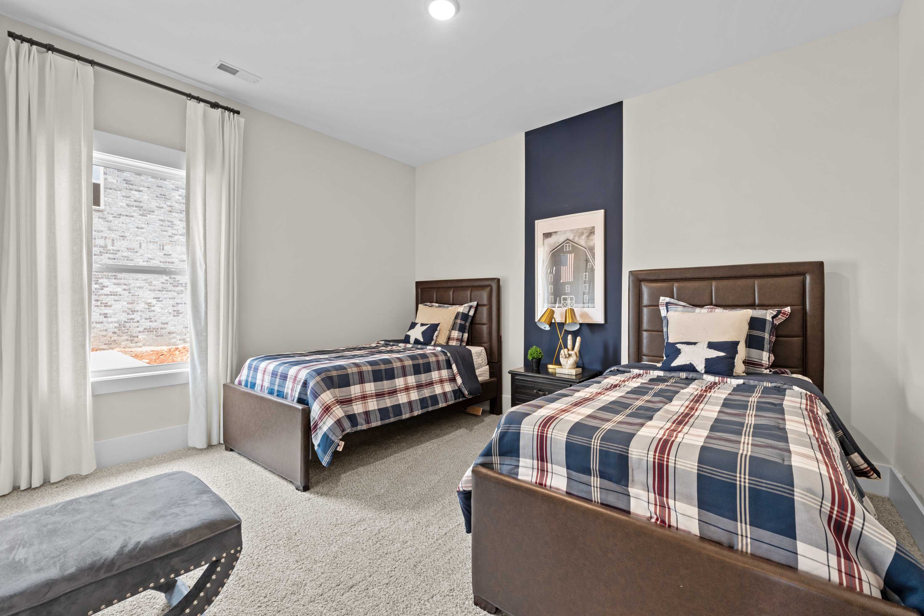 Cozy twin bedroom with navy accent wall, plaid bedding, and window drapes at Ivy Hills in Toney, Alabama