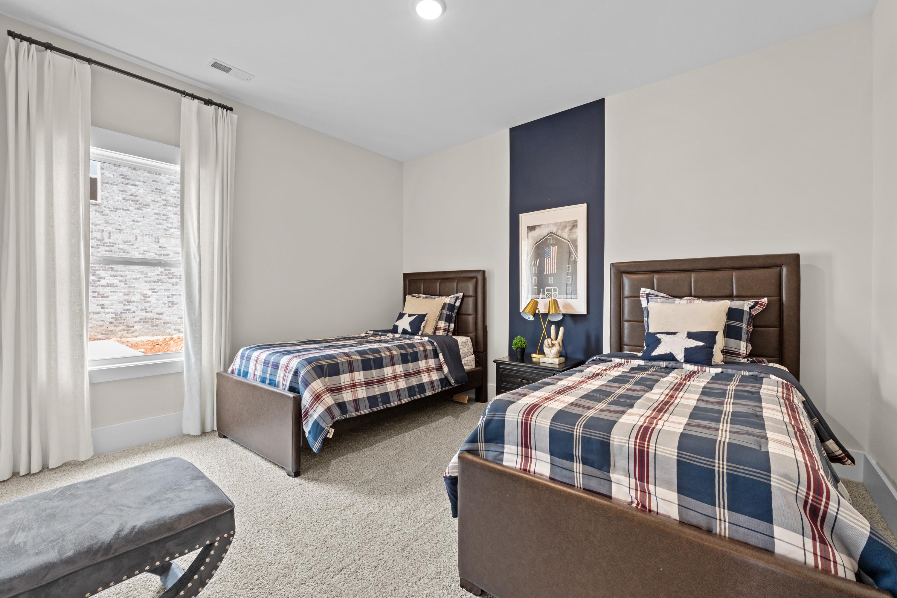 Cozy twin bedroom with navy accent wall, plaid bedding, and window drapes at Ivy Hills in Toney, Alabama