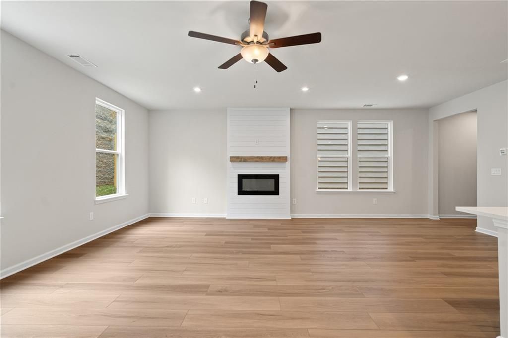 Cozy open-concept living room with white shiplap fireplace, hardwood floors, and ceiling fan in Davidson Homes The Marion B, Kennesaw, GA