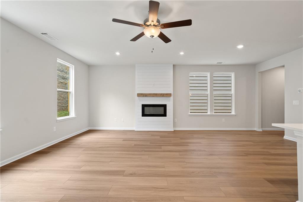 Cozy open-concept living room with white shiplap fireplace, hardwood floors, and ceiling fan in Davidson Homes The Marion B, Kennesaw, GA