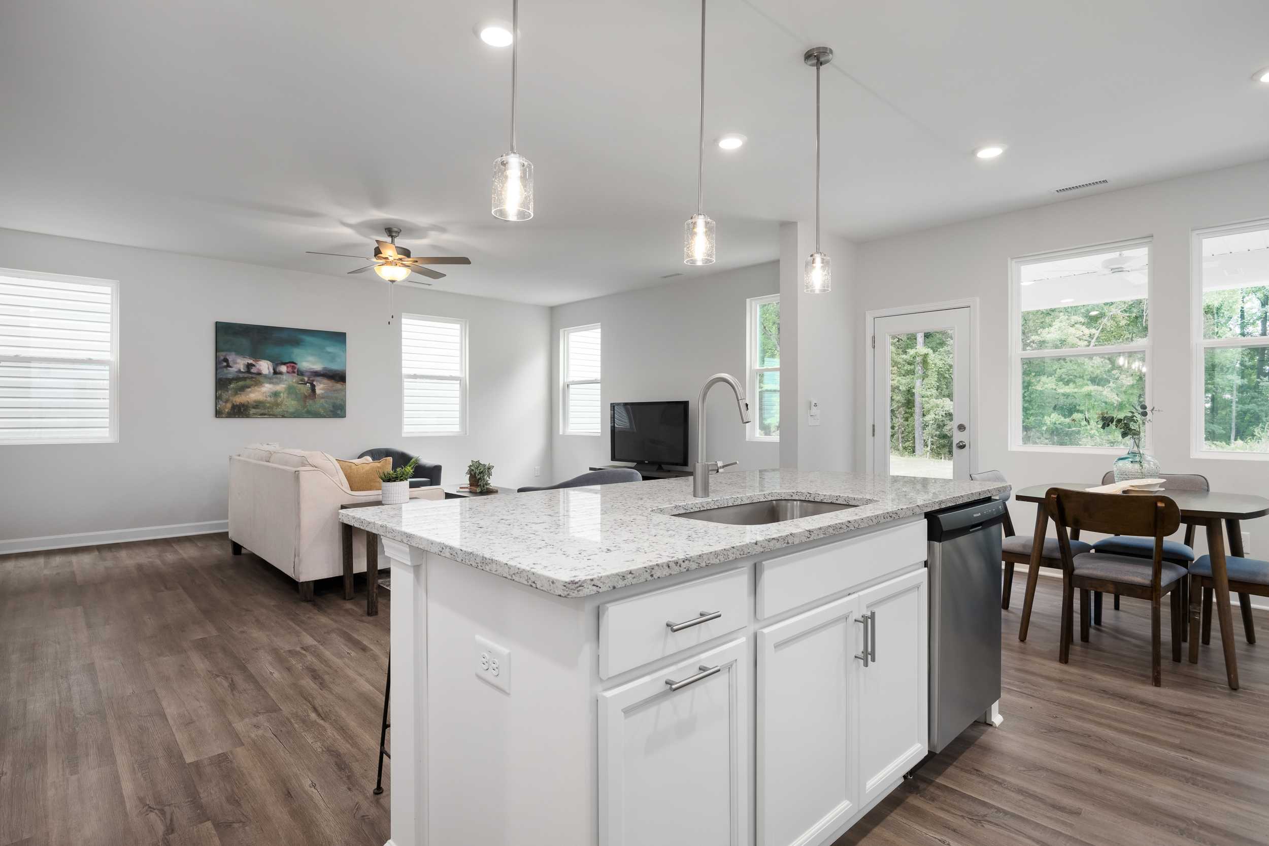 Open-concept kitchen and living room in Gregory Village Townhomes, Lillington NC with white cabinets, quartz island, hardwood floors, ceiling fan
