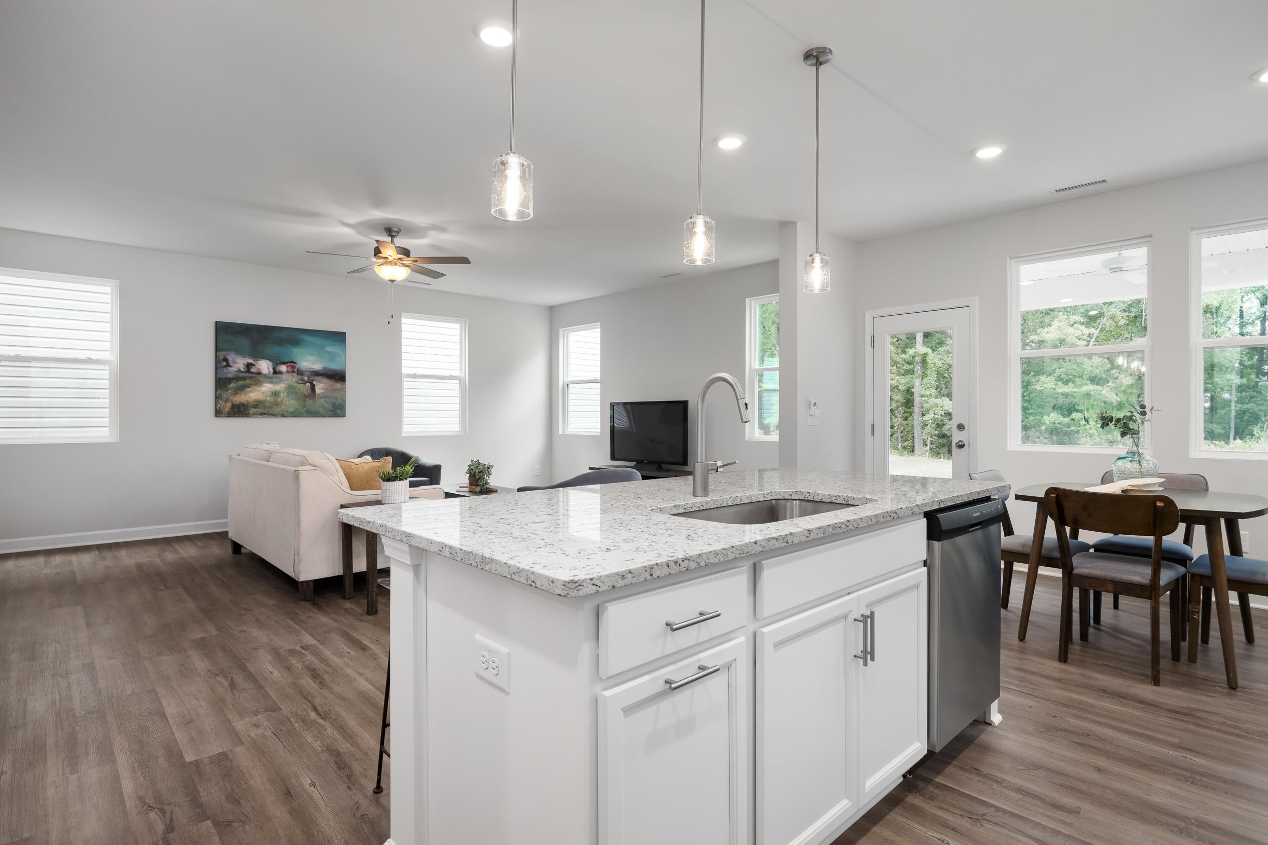 Open-concept kitchen and living room in Gregory Village Townhomes, Lillington NC with white cabinets, quartz island, hardwood floors, ceiling fan