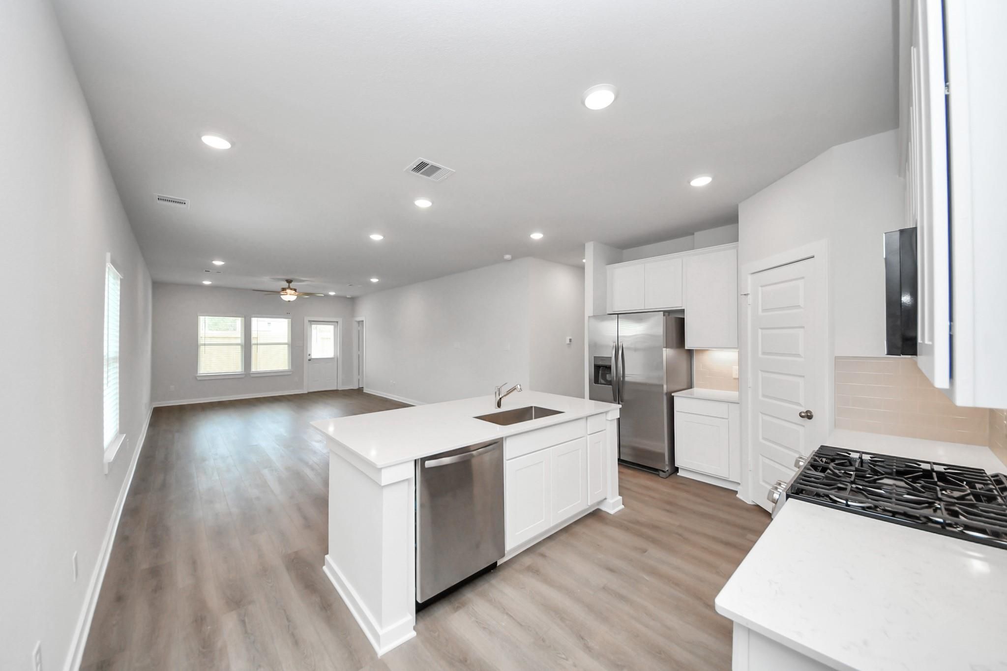 Open-concept kitchen with white cabinetry, island with sink, and stainless appliances in Davidson Homes' Sabine F plan, Conroe, TX