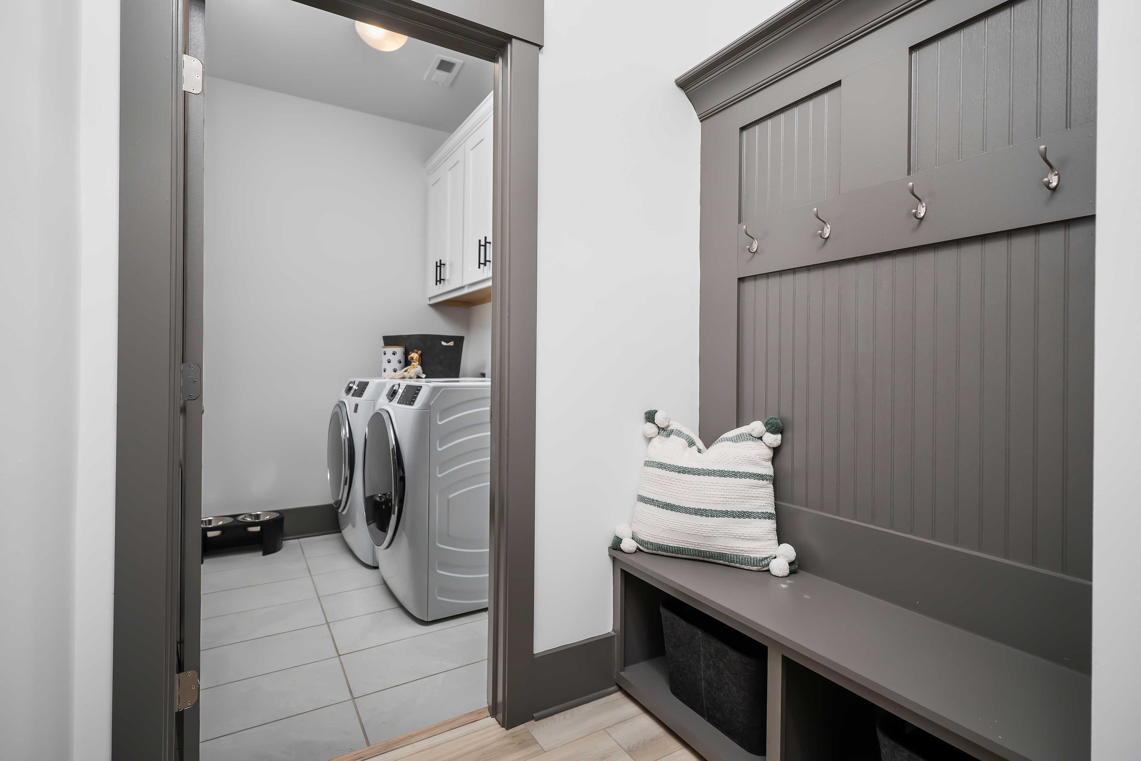 Laundry room and mudroom at Barnett's Crossing in Madison AL with white washer dryer, gray built-in bench, hooks, and cabinets