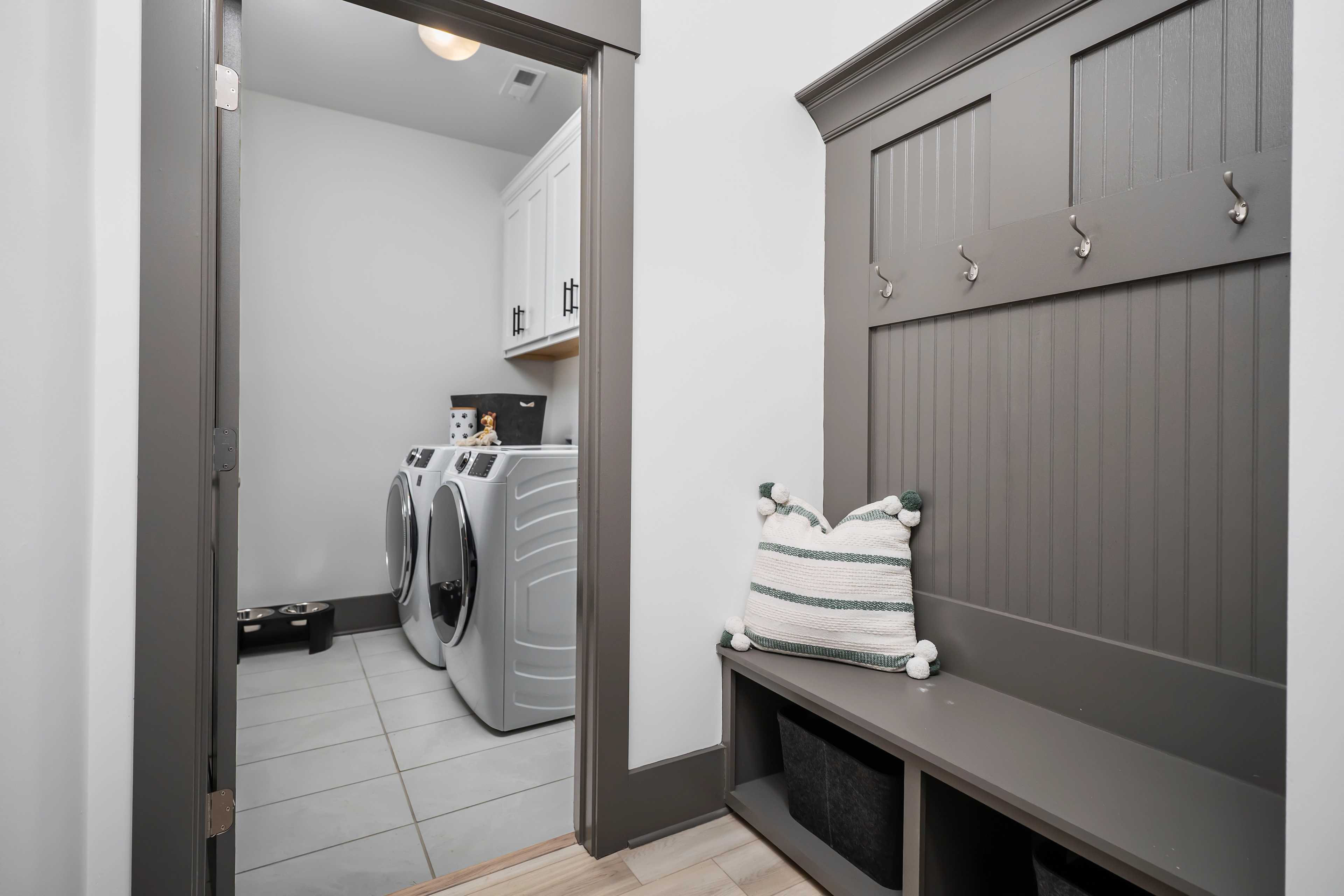 Laundry room and mudroom at Barnett's Crossing in Madison AL with white washer dryer, gray built-in bench, hooks, and cabinets