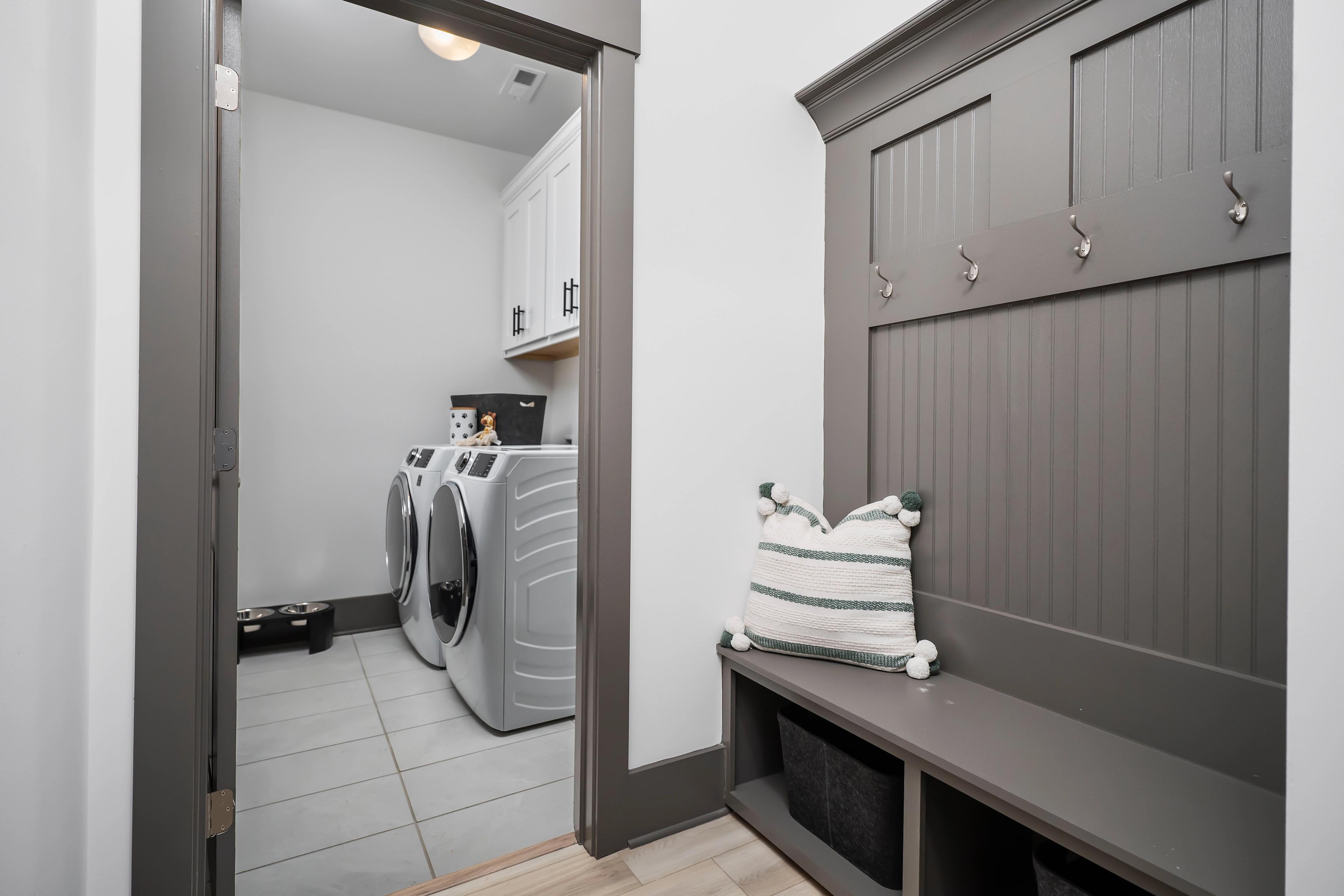 Laundry room and mudroom at Barnett's Crossing in Madison AL with white washer dryer, gray built-in bench, hooks, and cabinets