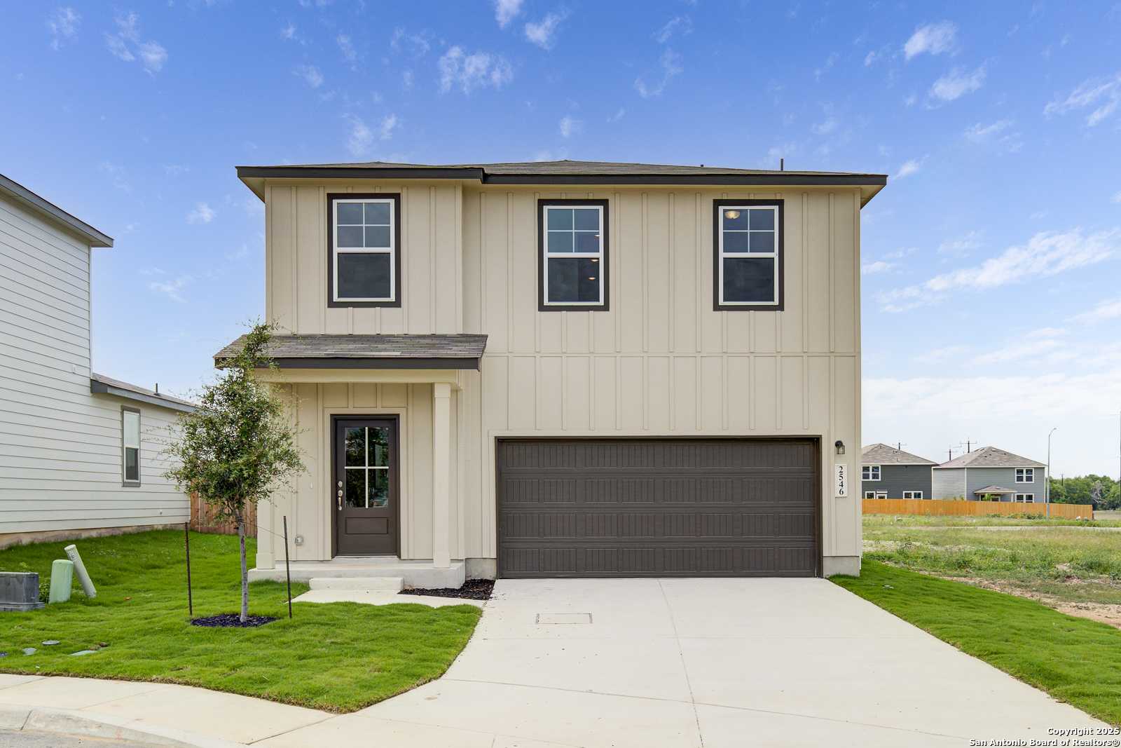 Modern two-story beige home with 2-car garage, front porch, and landscaped yard in Applewhite Meadows, San Antonio, Texas - Davidson Homes The Trinity A