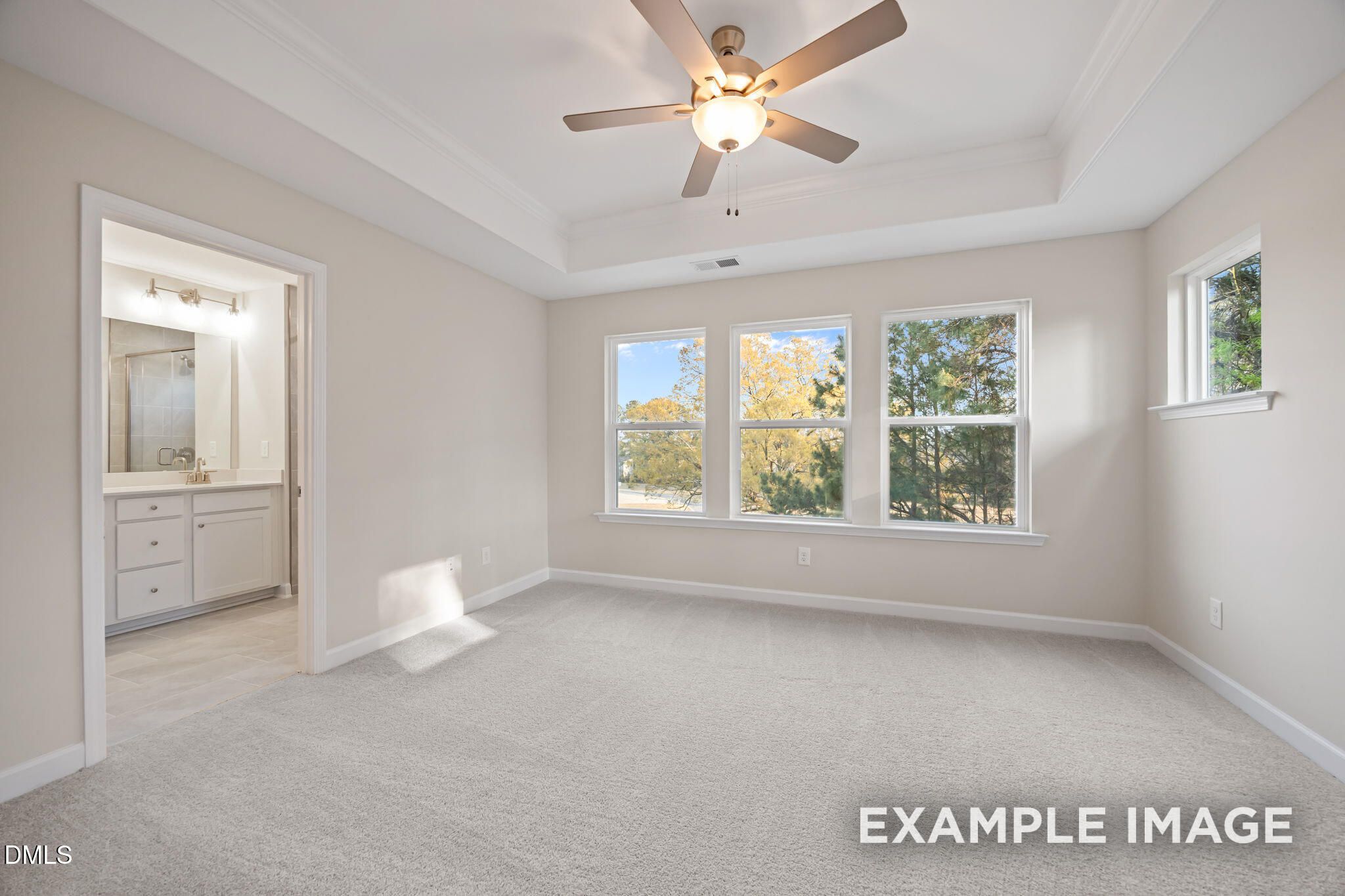 Spacious master bedroom with en-suite bath, ceiling fan, and large windows overlooking autumn trees in Davidson Homes The Avery, Knightdale, NC