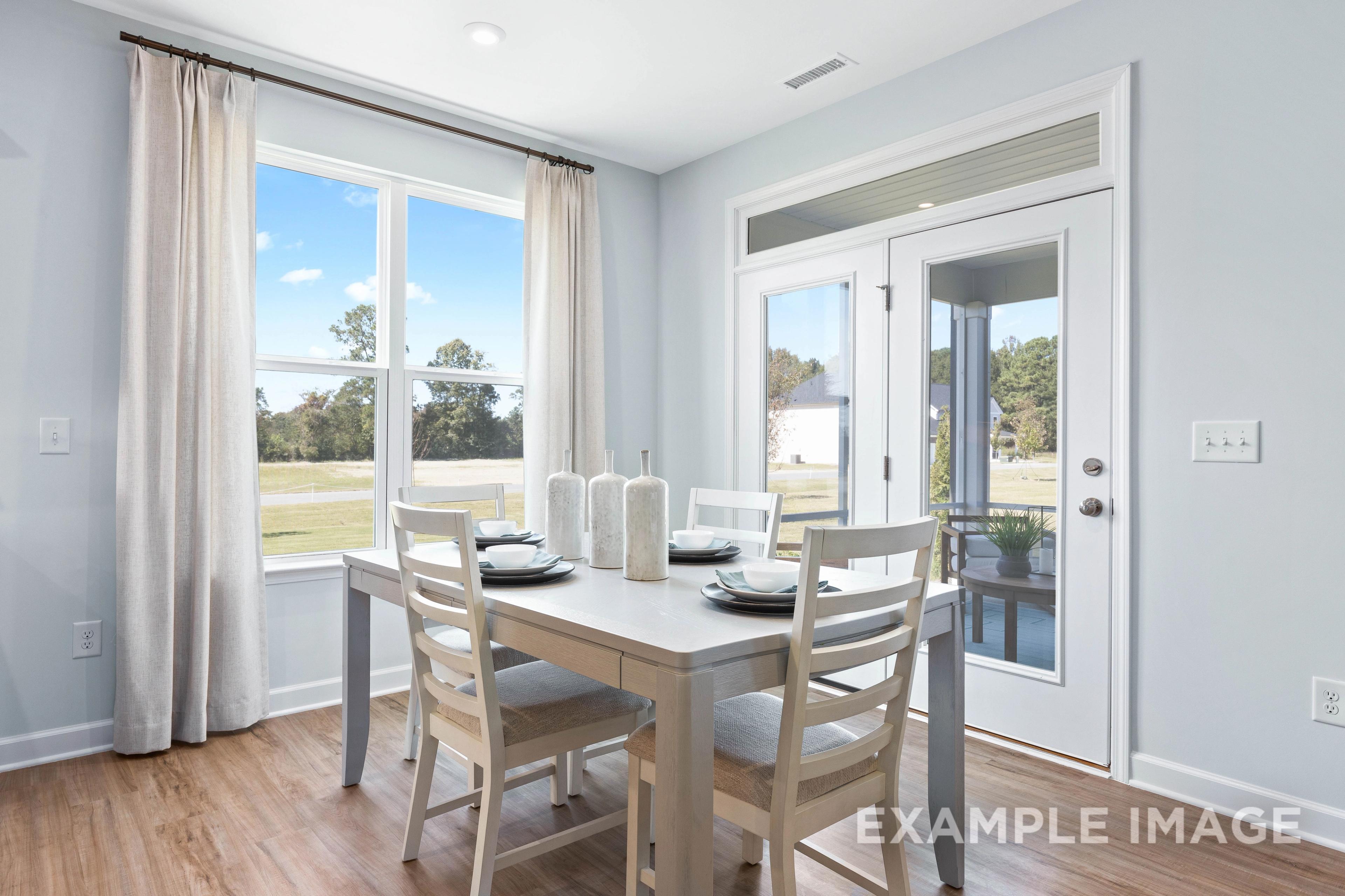 Spacious dining room in The Ash home design with set wooden table for four, French doors, and scenic field views through large windows