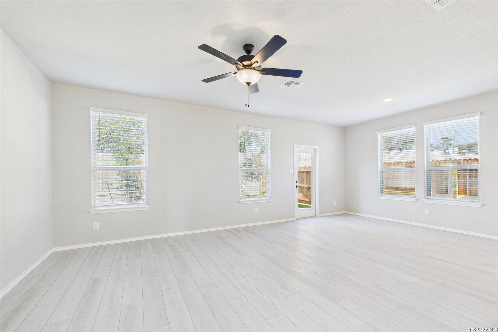 Bright spacious living room with large windows, ceiling fan, and light wood flooring in Davidson Homes The Charlotte A, San Antonio