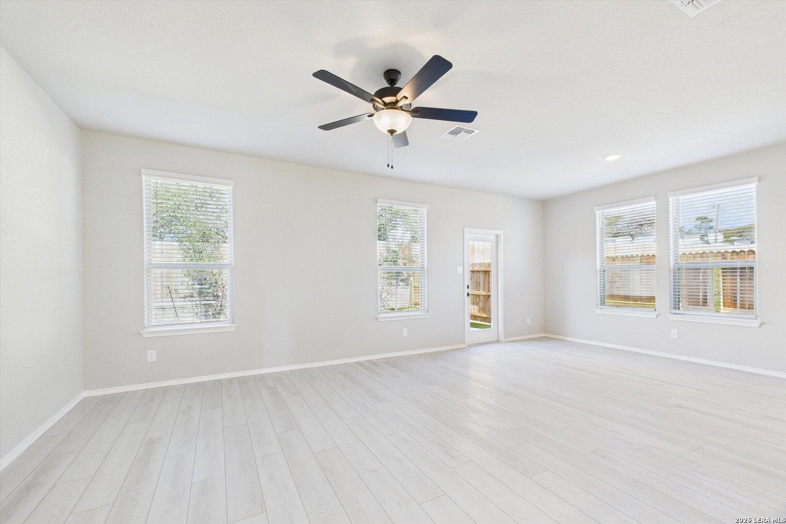 Bright spacious living room with large windows, ceiling fan, and light wood flooring in Davidson Homes The Charlotte A, San Antonio