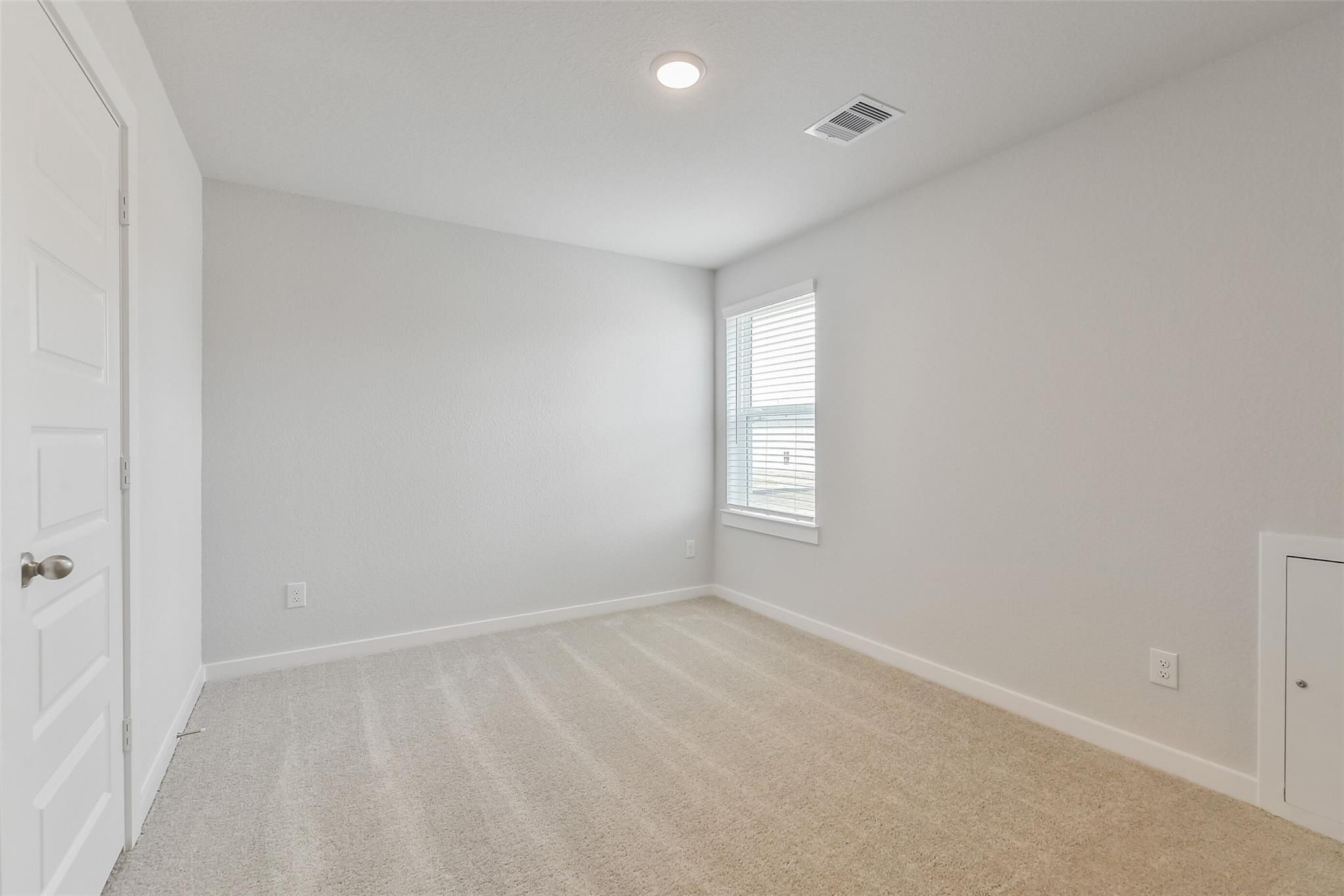 Bright secondary bedroom featuring light gray walls, beige carpet, and window blinds in Davidson Homes The Brazos E, Cleveland, Texas
