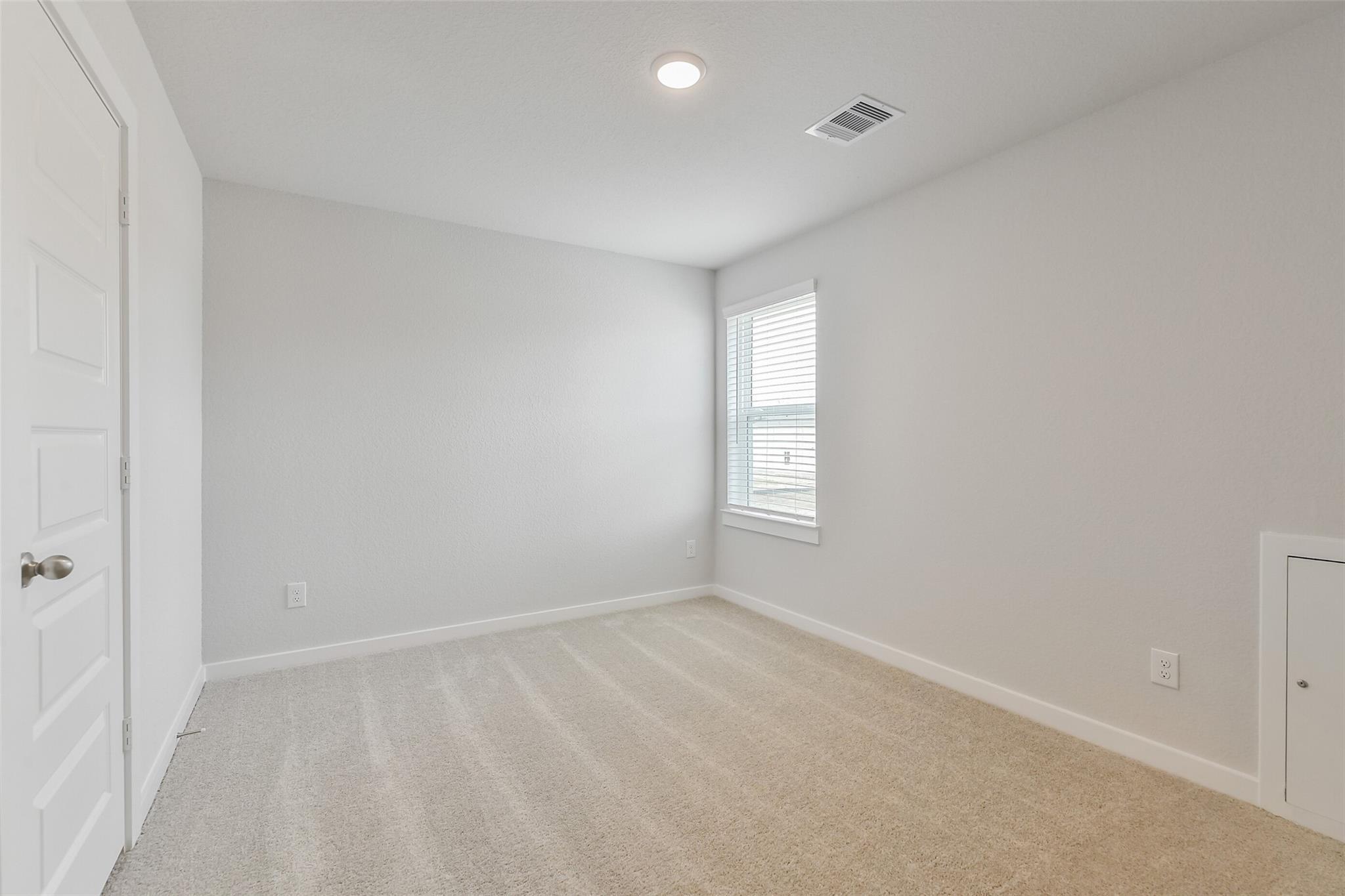 Bright secondary bedroom featuring light gray walls, beige carpet, and window blinds in Davidson Homes The Brazos E, Cleveland, Texas