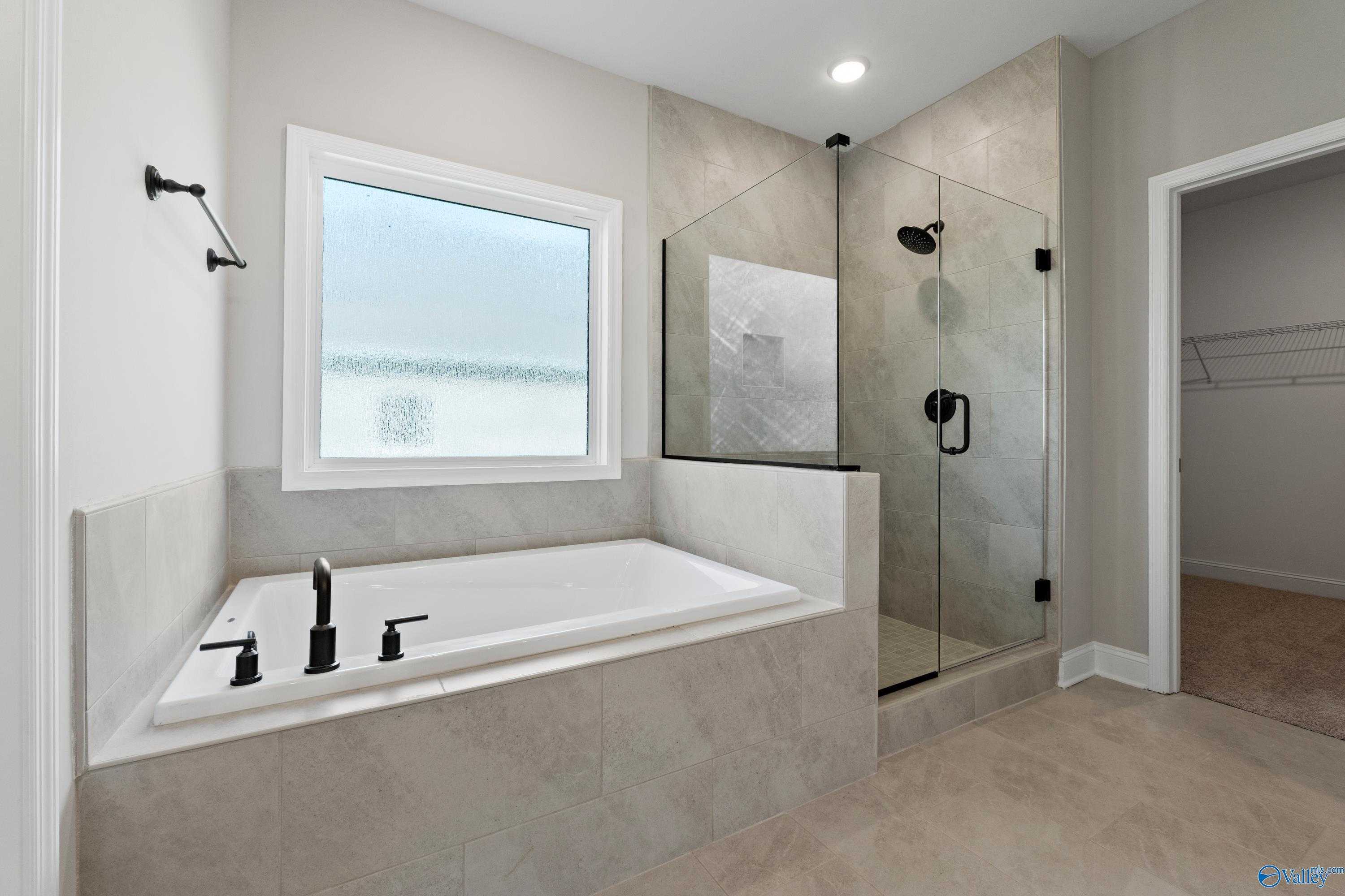 Luxurious master bathroom with freestanding tub, frameless glass shower, and neutral tiles in Davidson Homes The Rockford, Toney, AL