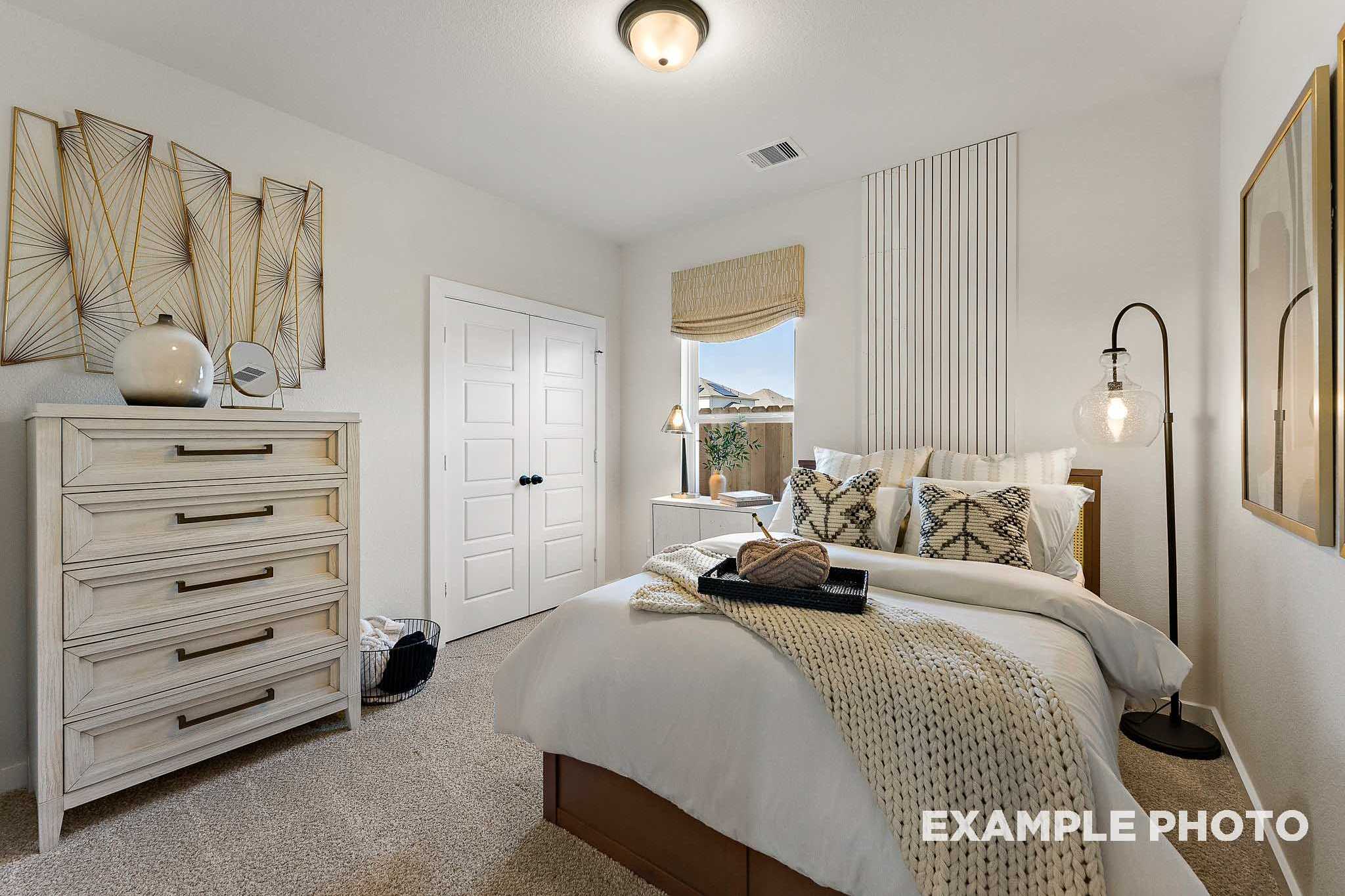 Spacious master bedroom in The Everett E showcasing king bed with white bedding, wooden dresser, arched lamp, and neutral decor