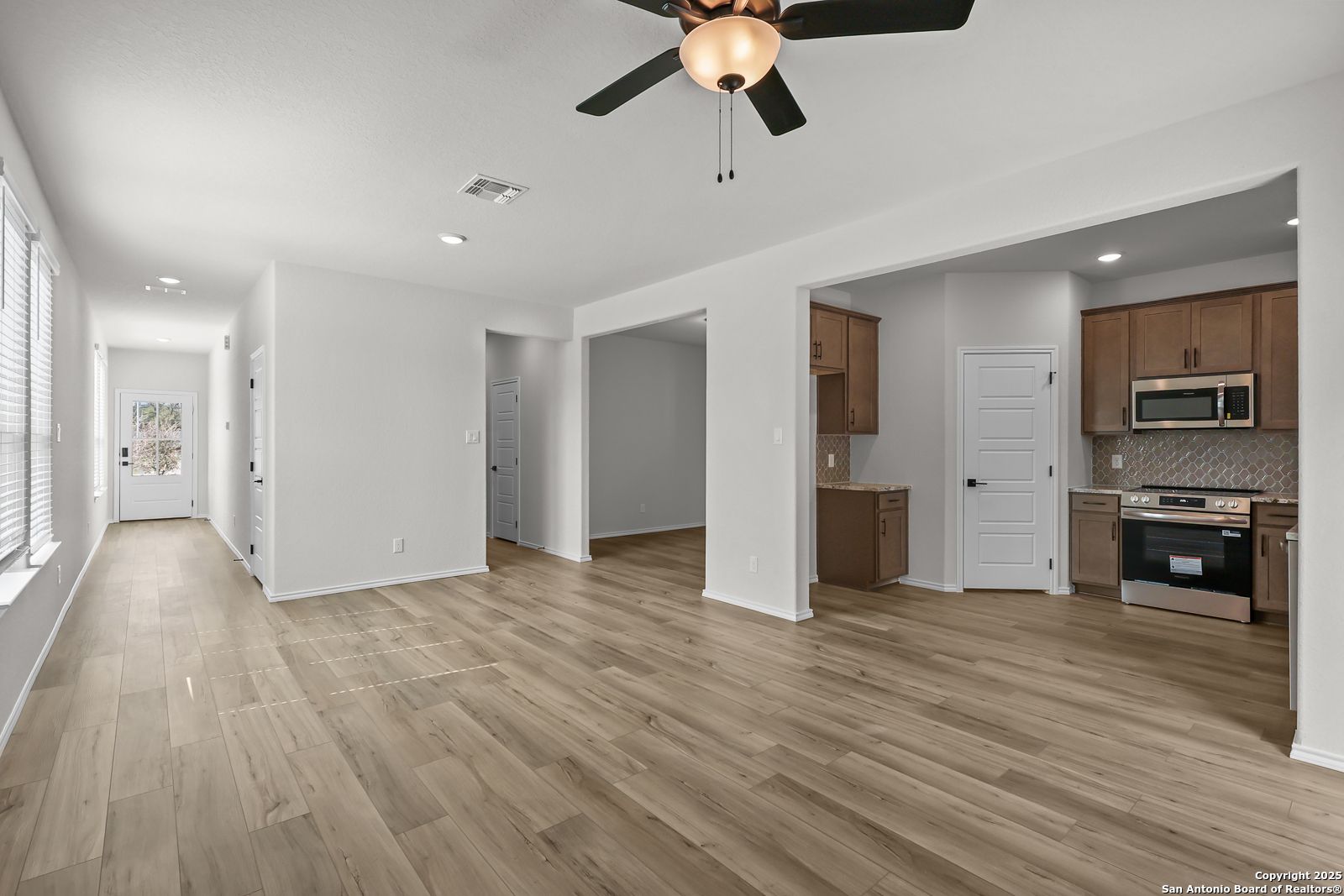 Spacious open hallway with hardwood floors leading to modern kitchen with stainless appliances in Davidson Homes The Florence C, San Antonio