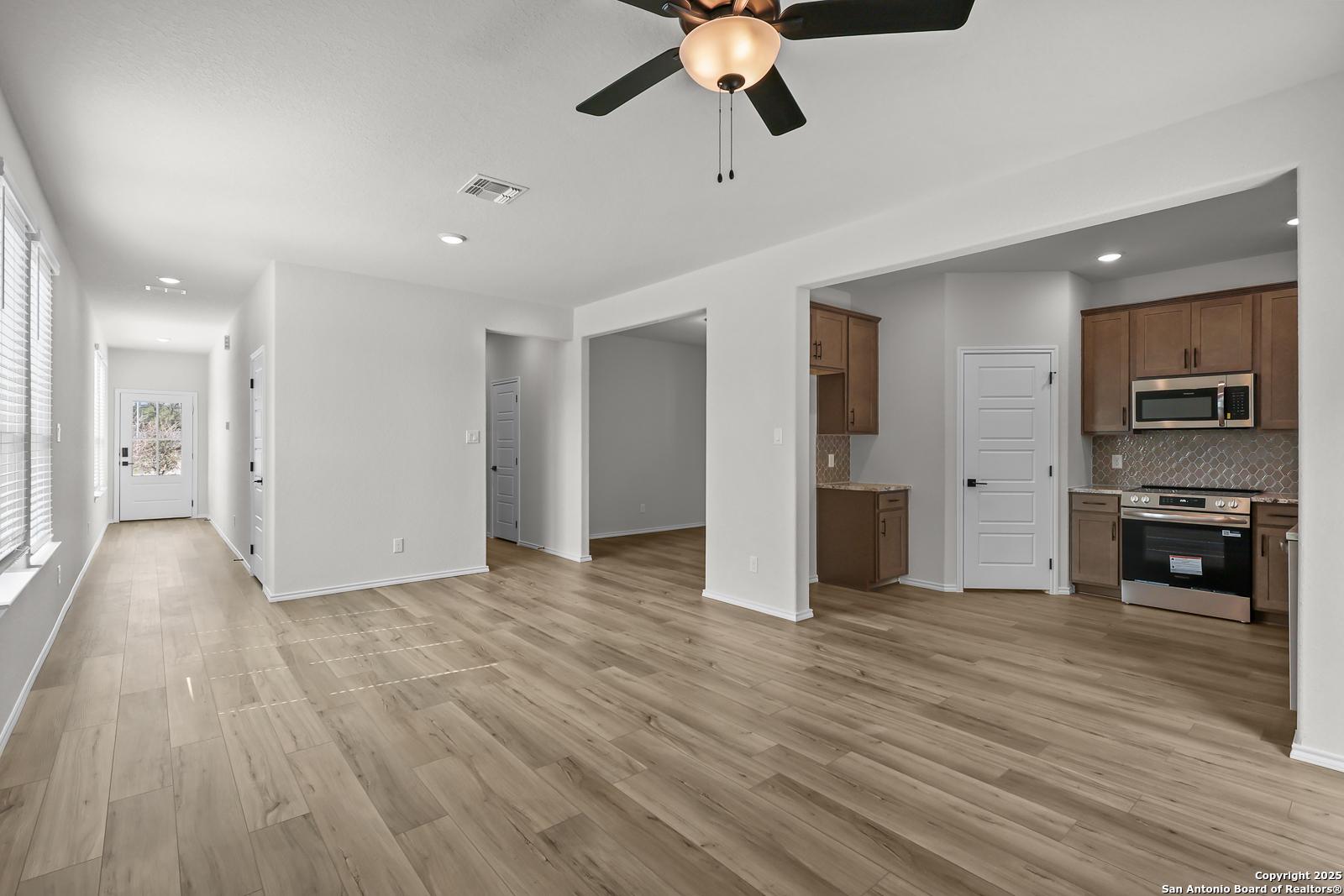 Spacious open hallway with hardwood floors leading to modern kitchen with stainless appliances in Davidson Homes The Florence C, San Antonio