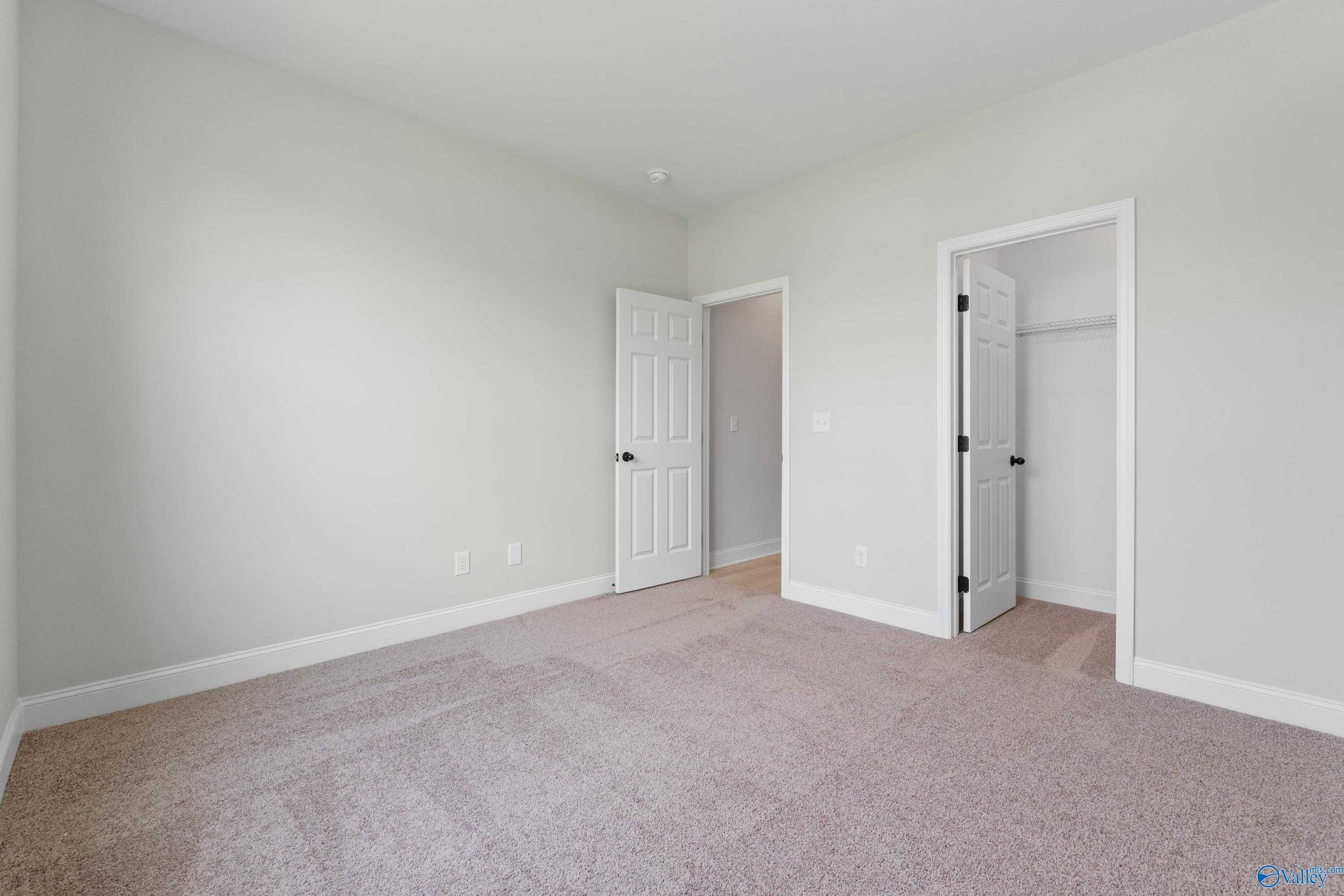 Spacious secondary bedroom with walk-in closet, neutral gray walls, and beige carpet in Davidson Homes The Kirkland, Harvest AL