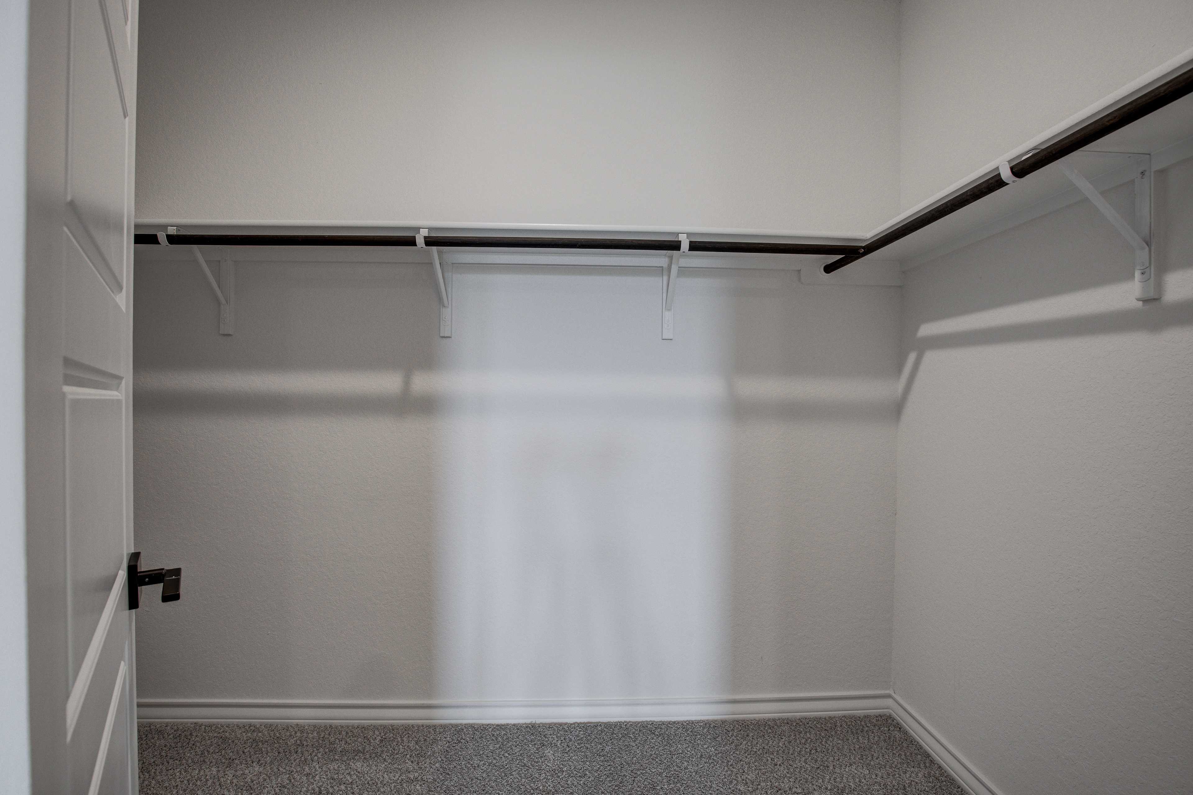 Spacious walk-in master closet in The Lanier by Davidson Homes featuring white walls, wooden hanging rods, built-in shelves, and carpeted floor