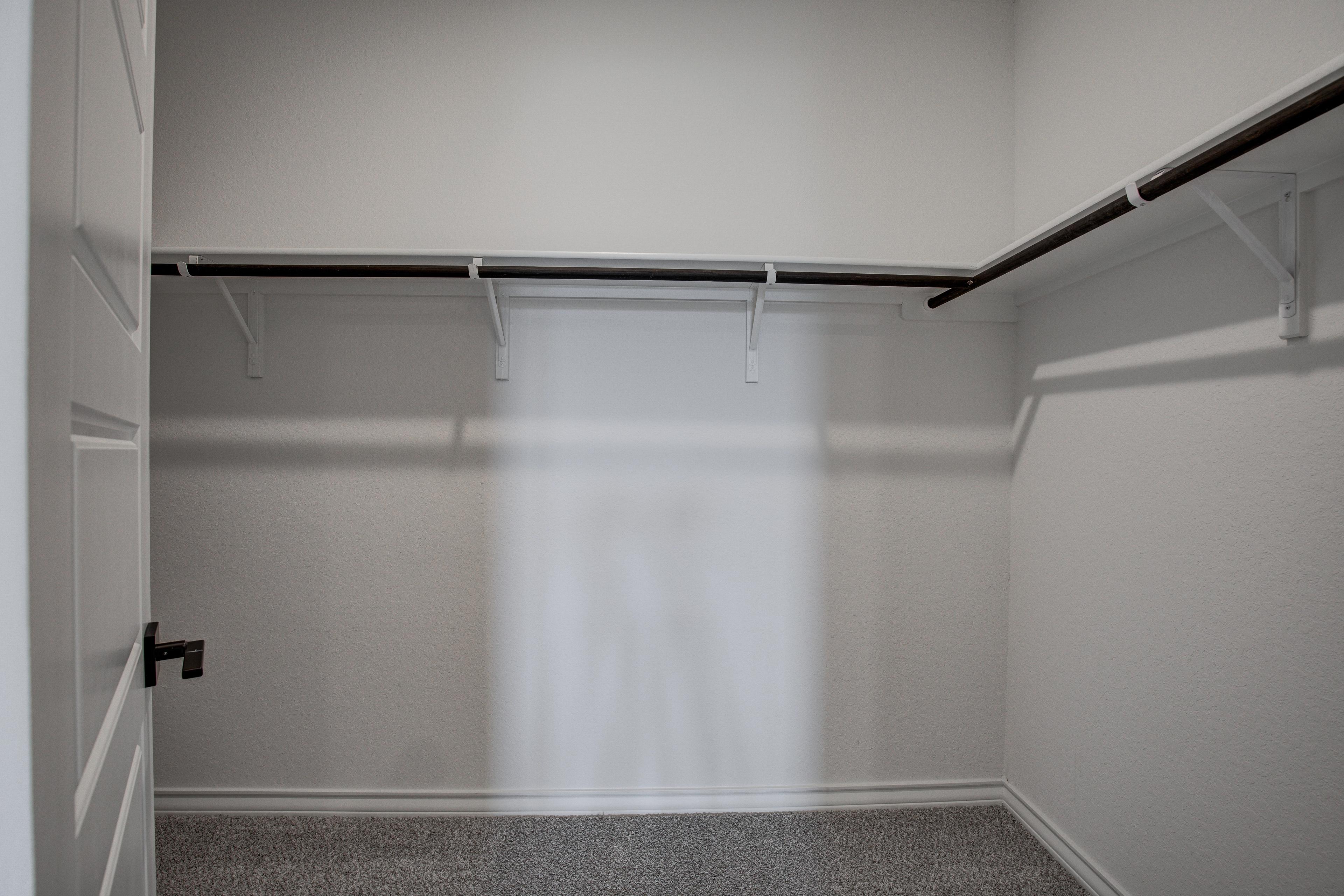 Spacious walk-in master closet in The Lanier home featuring white walls, wooden rods on brackets, neutral carpet, and open door
