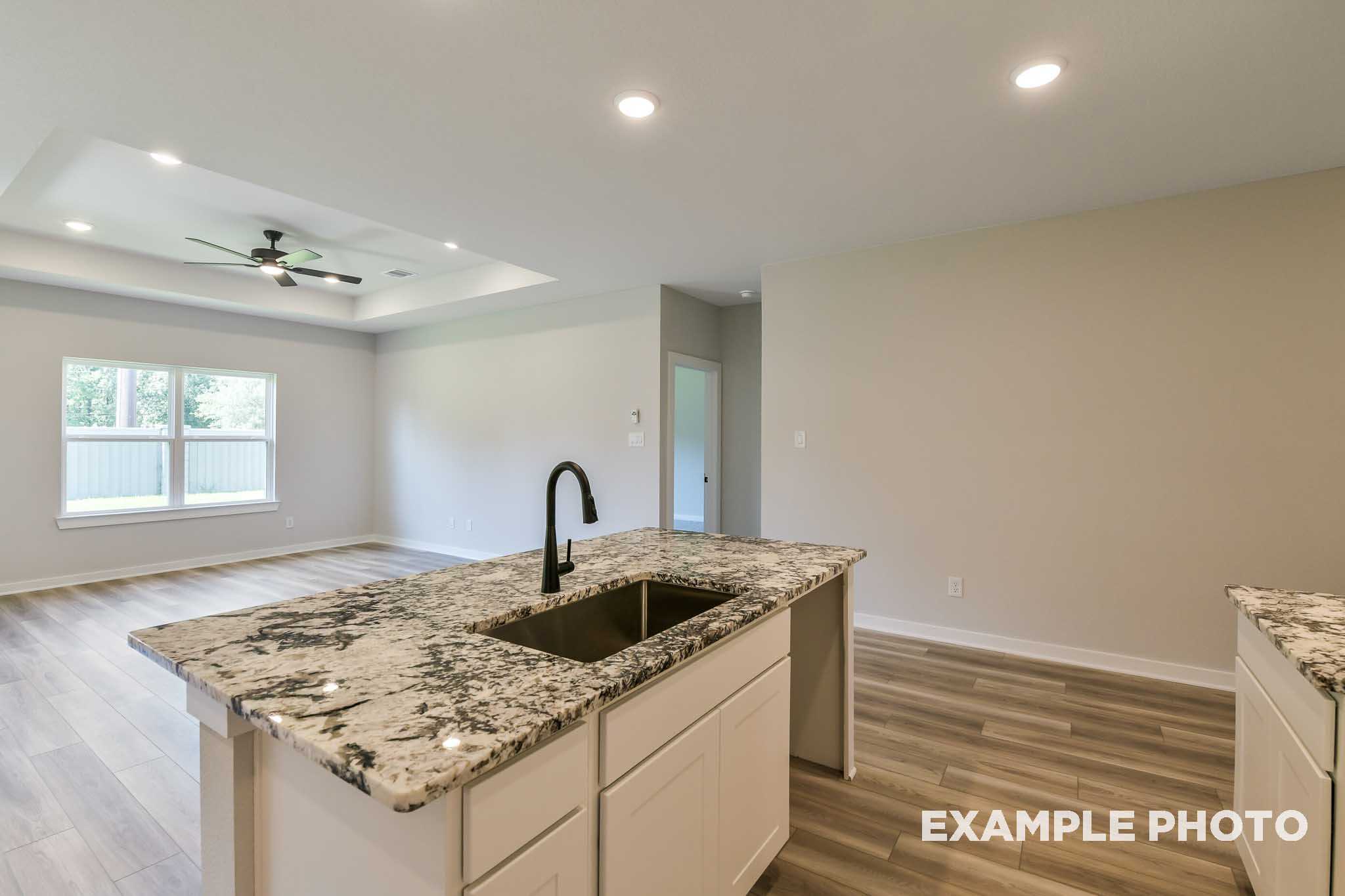 Spacious open-concept kitchen in The Daphne G Davidson Homes design featuring large granite island, white cabinets, and matte black faucet