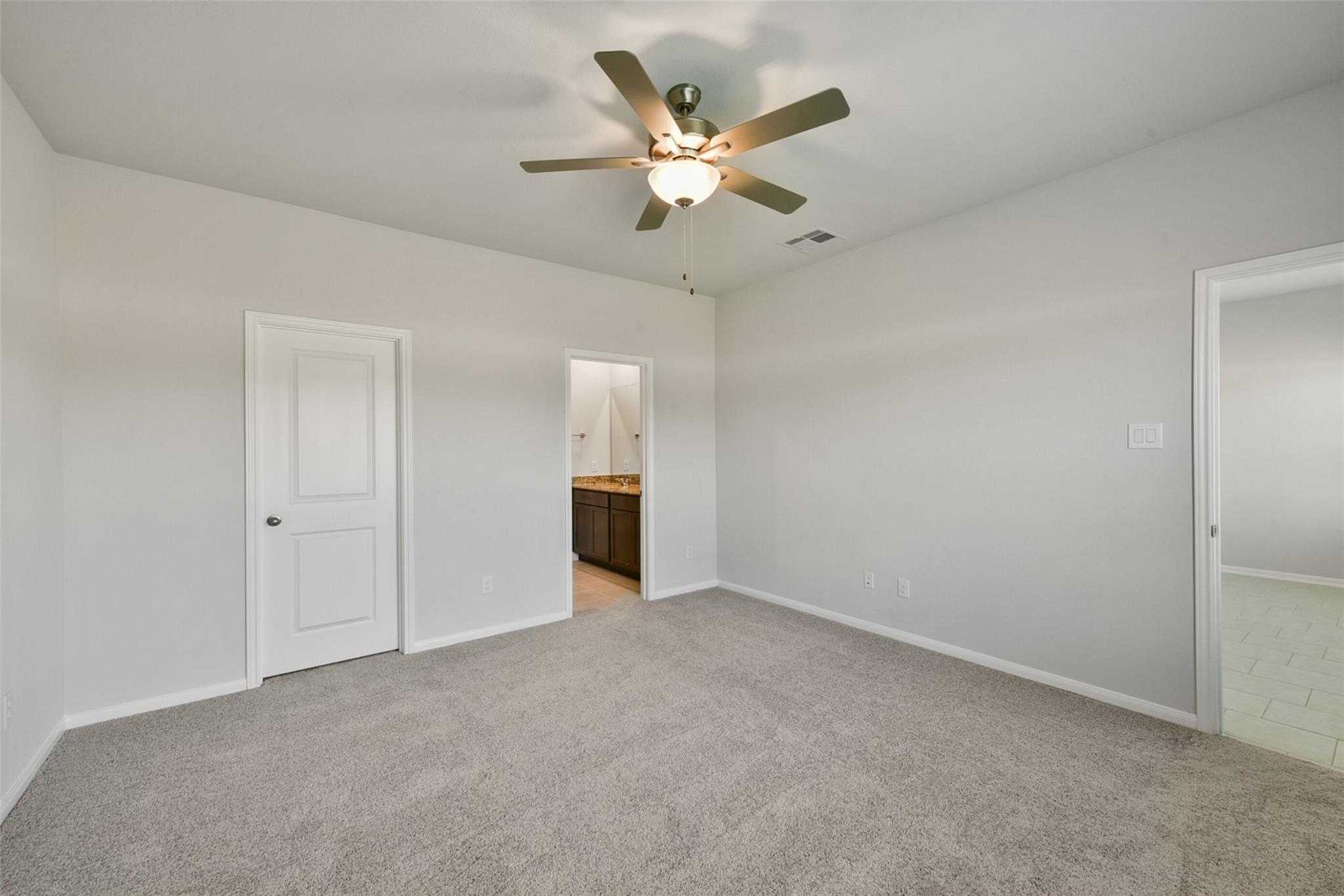 Spacious bedroom with gray carpet, ceiling fan, and attached bath vanity in Davidson Homes The Sabine E, Dayton, Texas