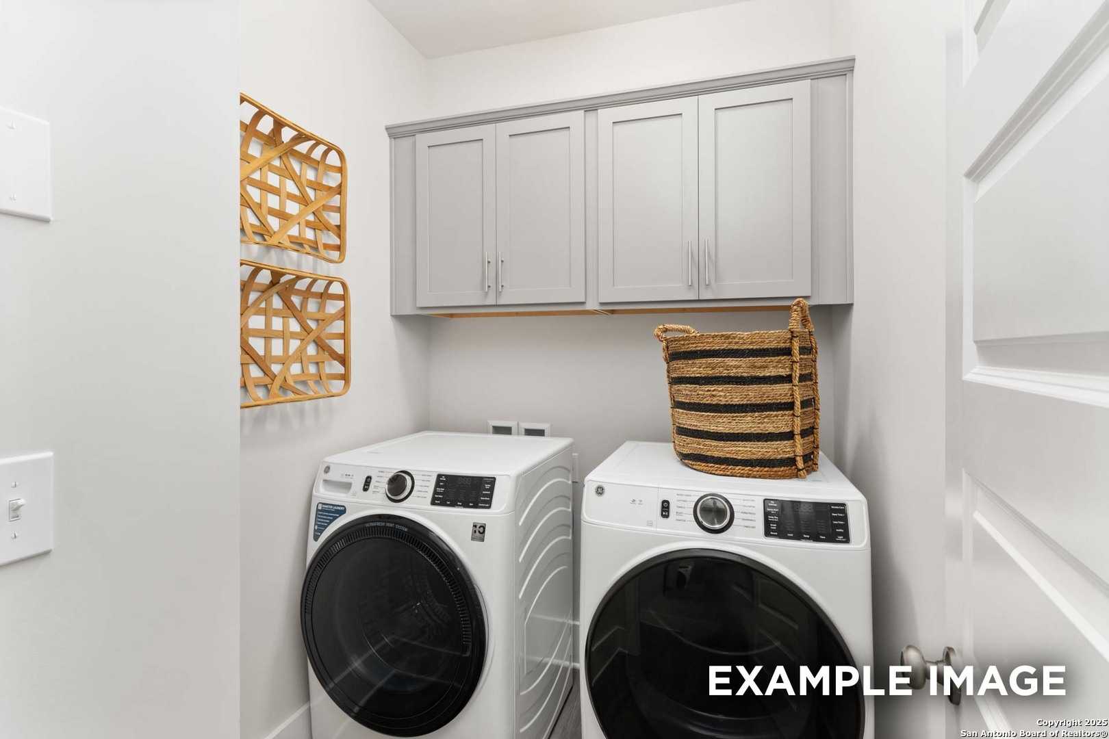Modern laundry room with white front-load washer dryer, gray cabinets, wicker baskets in Davidson Homes The Daphne H, Seguin, Texas