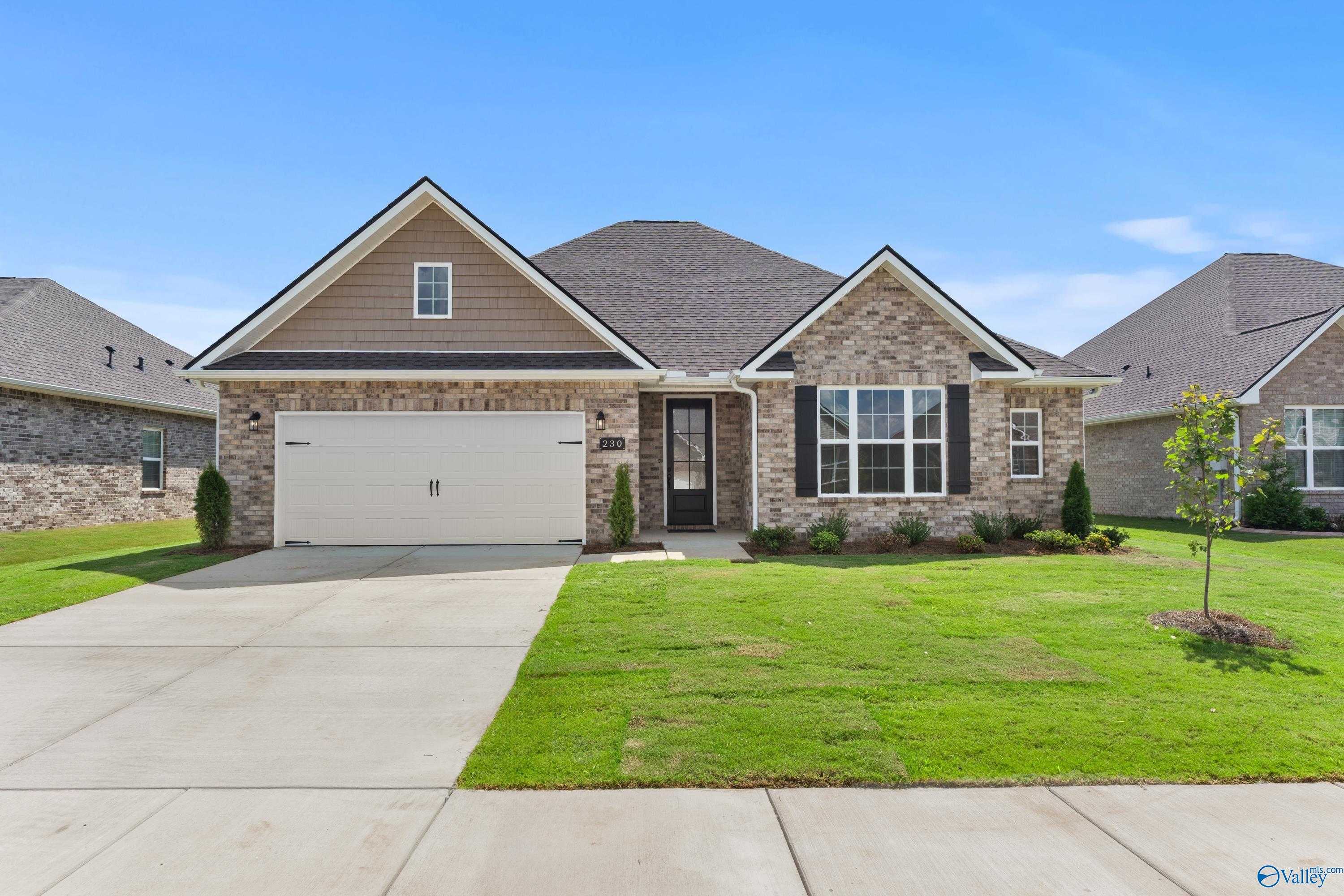 Charming 1.5-story brick home with 2-car garage, black door, and lush green lawn in Kendall Downs, Toney, Alabama