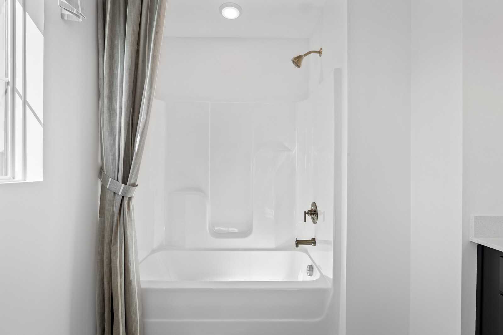 Clean white bathtub-shower combo with bronze fixtures, beige curtain, and vanity in Davidson Homes The Cumberland B bathroom, Gallatin, TN