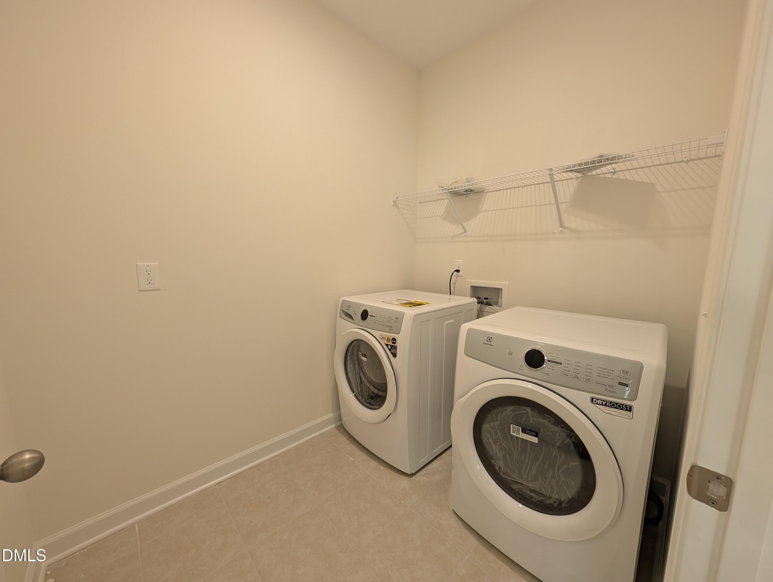 Laundry room with white front-load washer and dryer, tile flooring, and wire shelving in Davidson Homes The Magnolia A, Wendell NC