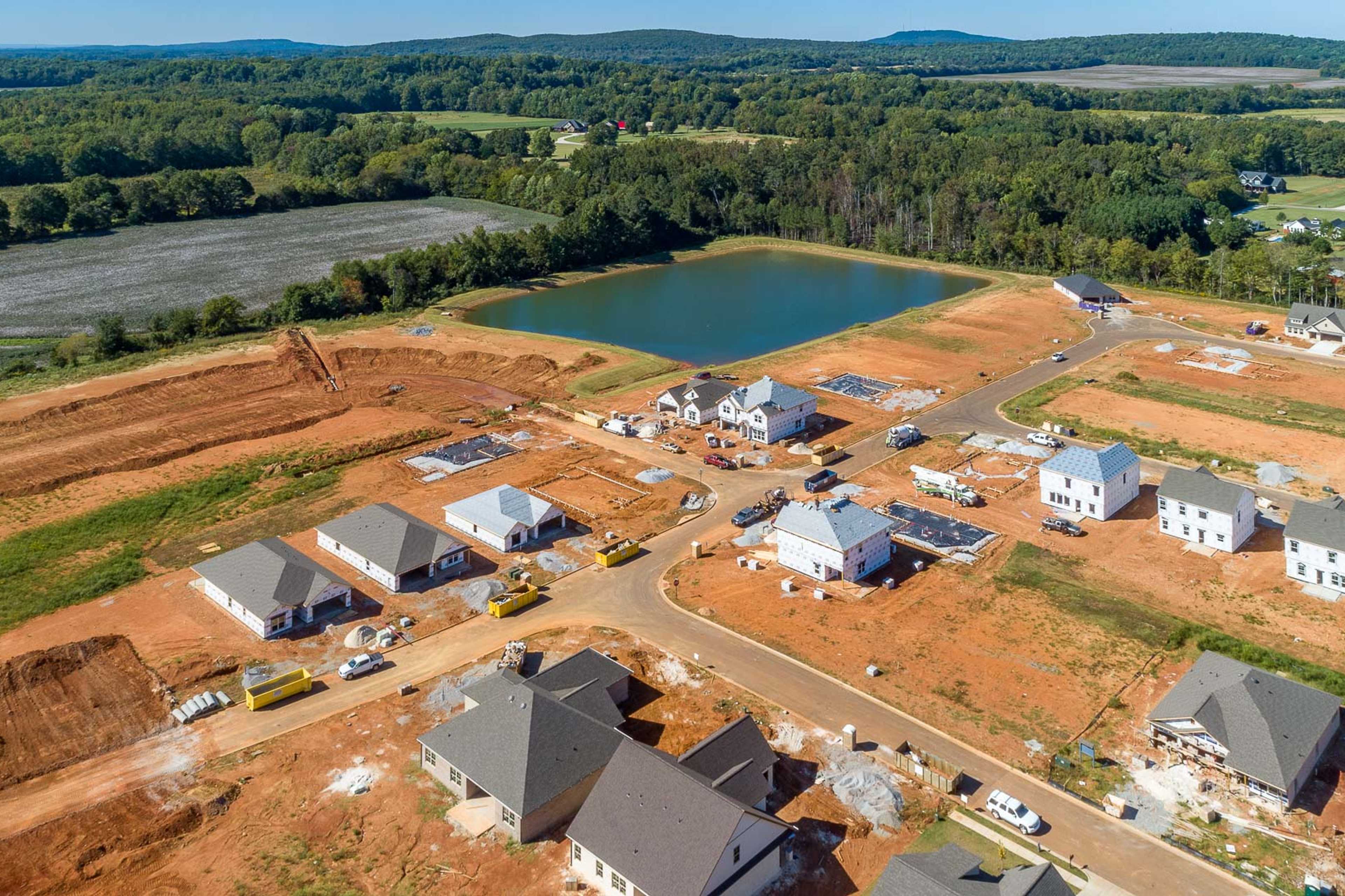 Aerial view of new homes under construction at Ivy Hills in Toney Alabama with pond wooded surroundings and red dirt lots
