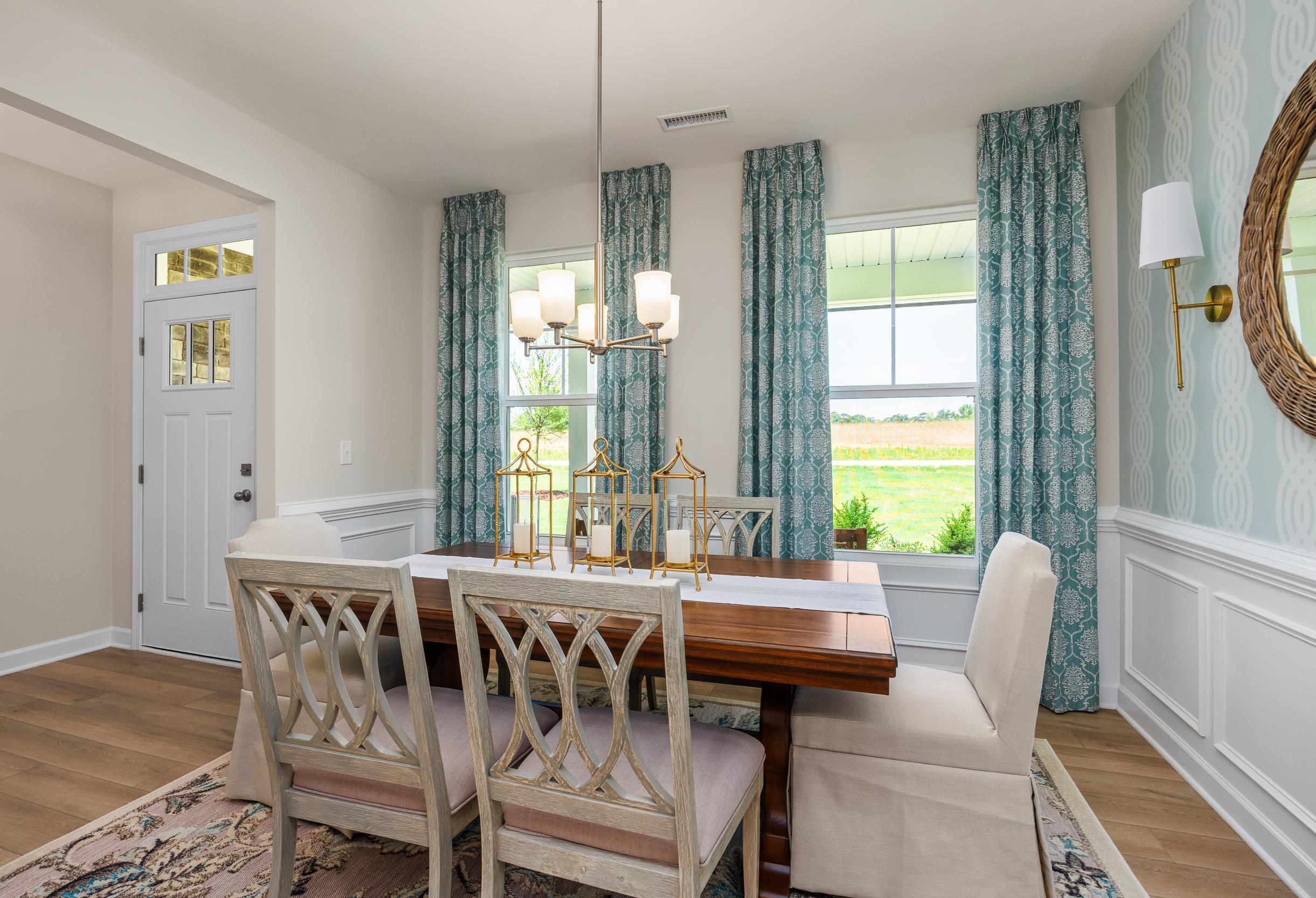 Bright dining room in The Willow B featuring elegant wood furniture, teal patterned curtains, and wainscoting detail.