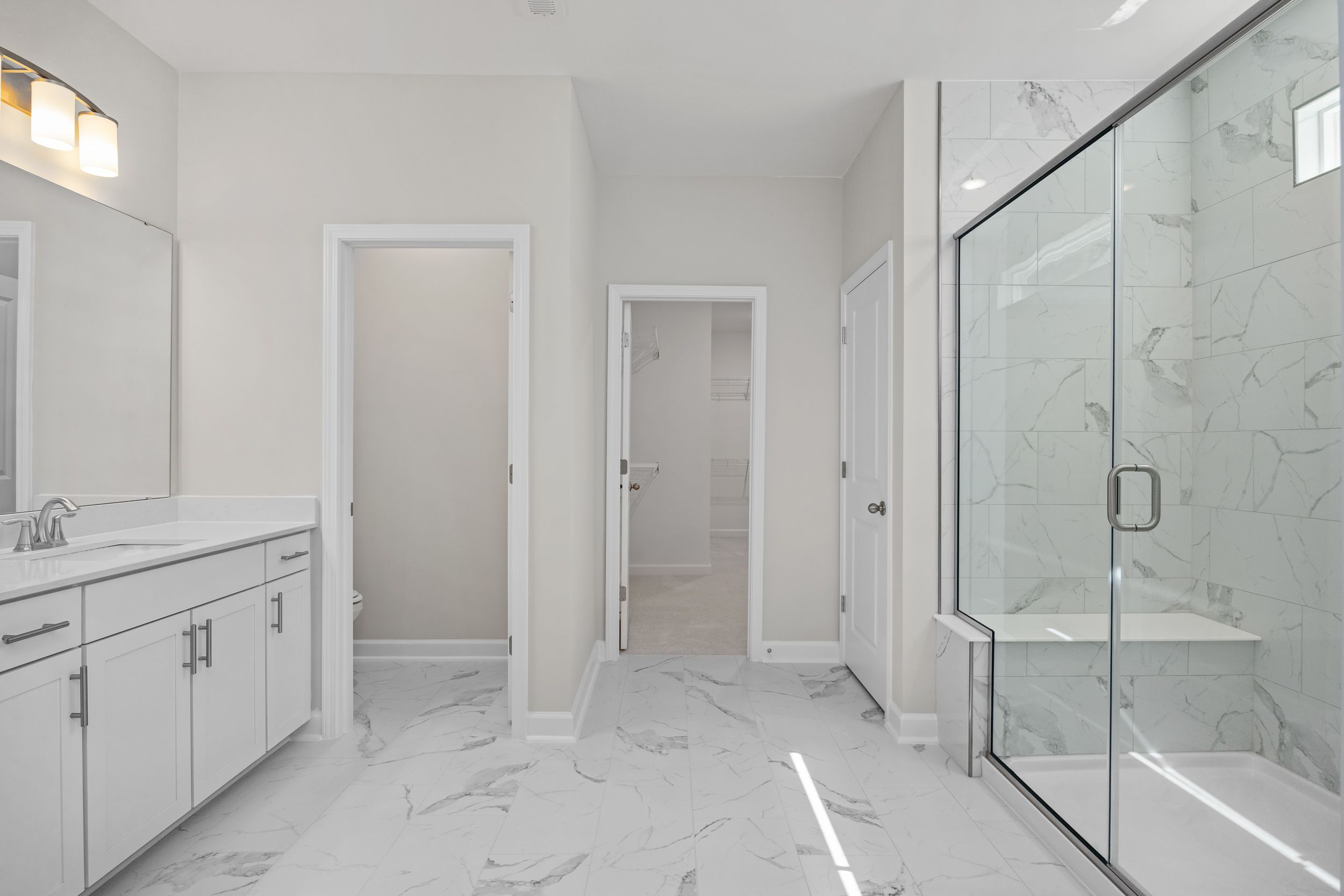 Spacious master bathroom in The Aspen C with double vanity, frameless glass shower, marble tiles, and white cabinetry