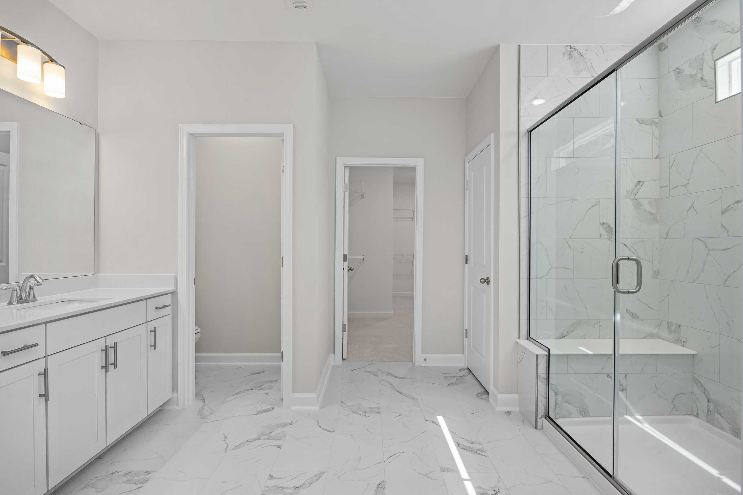 Spacious master bathroom in The Aspen C with double vanity, frameless glass shower, marble tiles, and white cabinetry