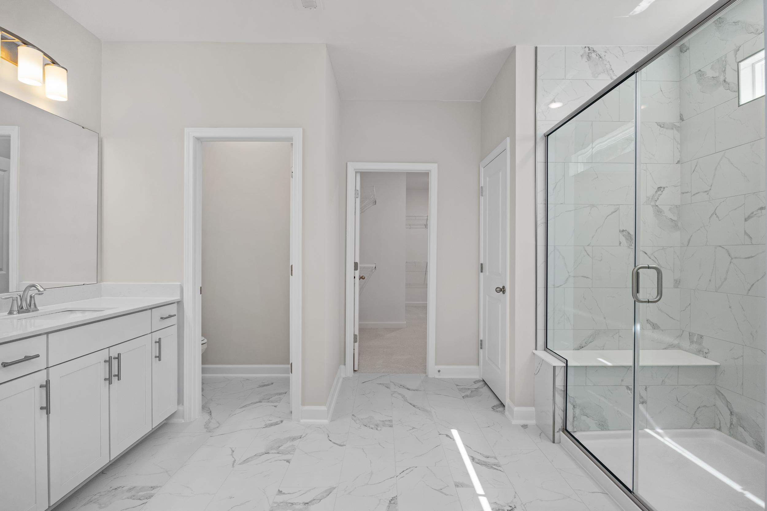 Spacious master bathroom in The Aspen C with double vanity, frameless glass shower, marble tiles, and white cabinetry