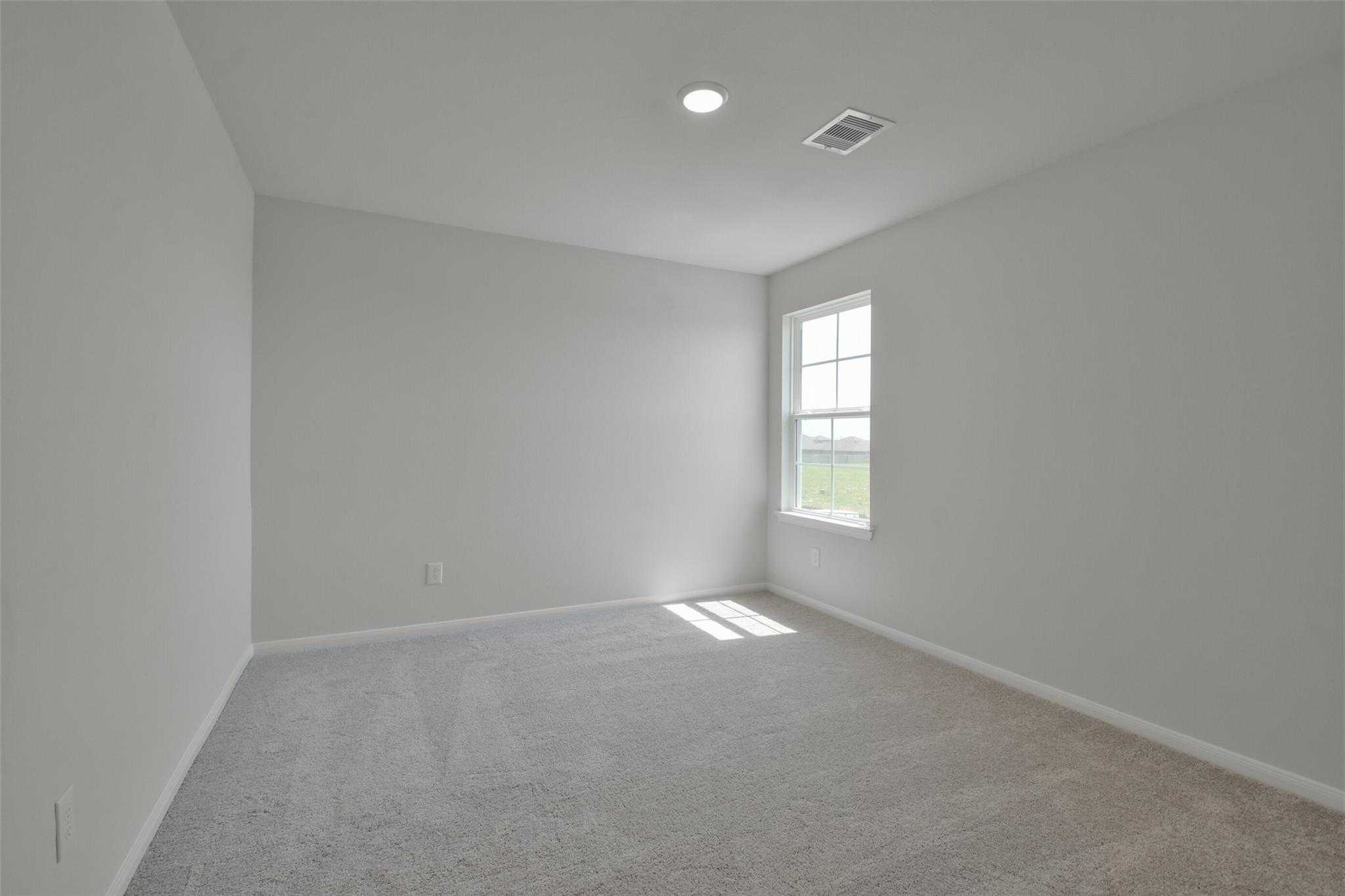 Empty secondary bedroom featuring gray walls, beige carpet, and sunlit window in Davidson Homes The Tierra A, Dayton, Texas