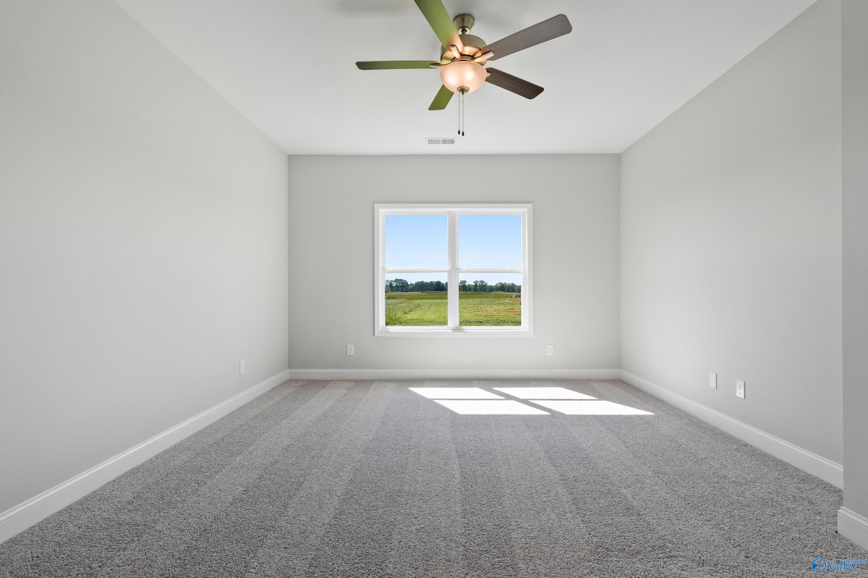 Bright empty bedroom with ceiling fan, large window overlooking green field in Davidson Homes The Everett, Hazel Green, AL
