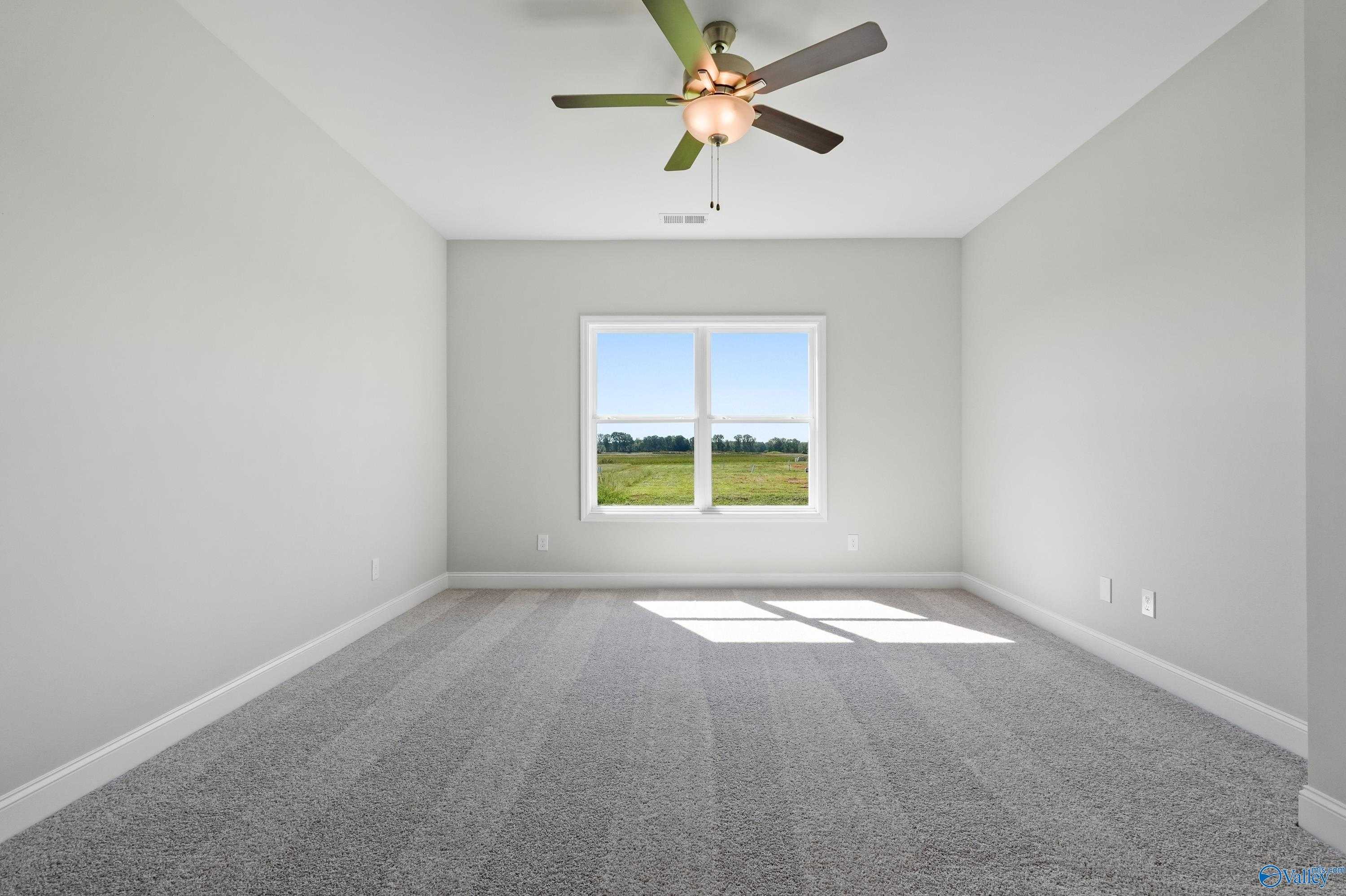 Bright empty bedroom with ceiling fan, large window overlooking green field in Davidson Homes The Everett, Hazel Green, AL