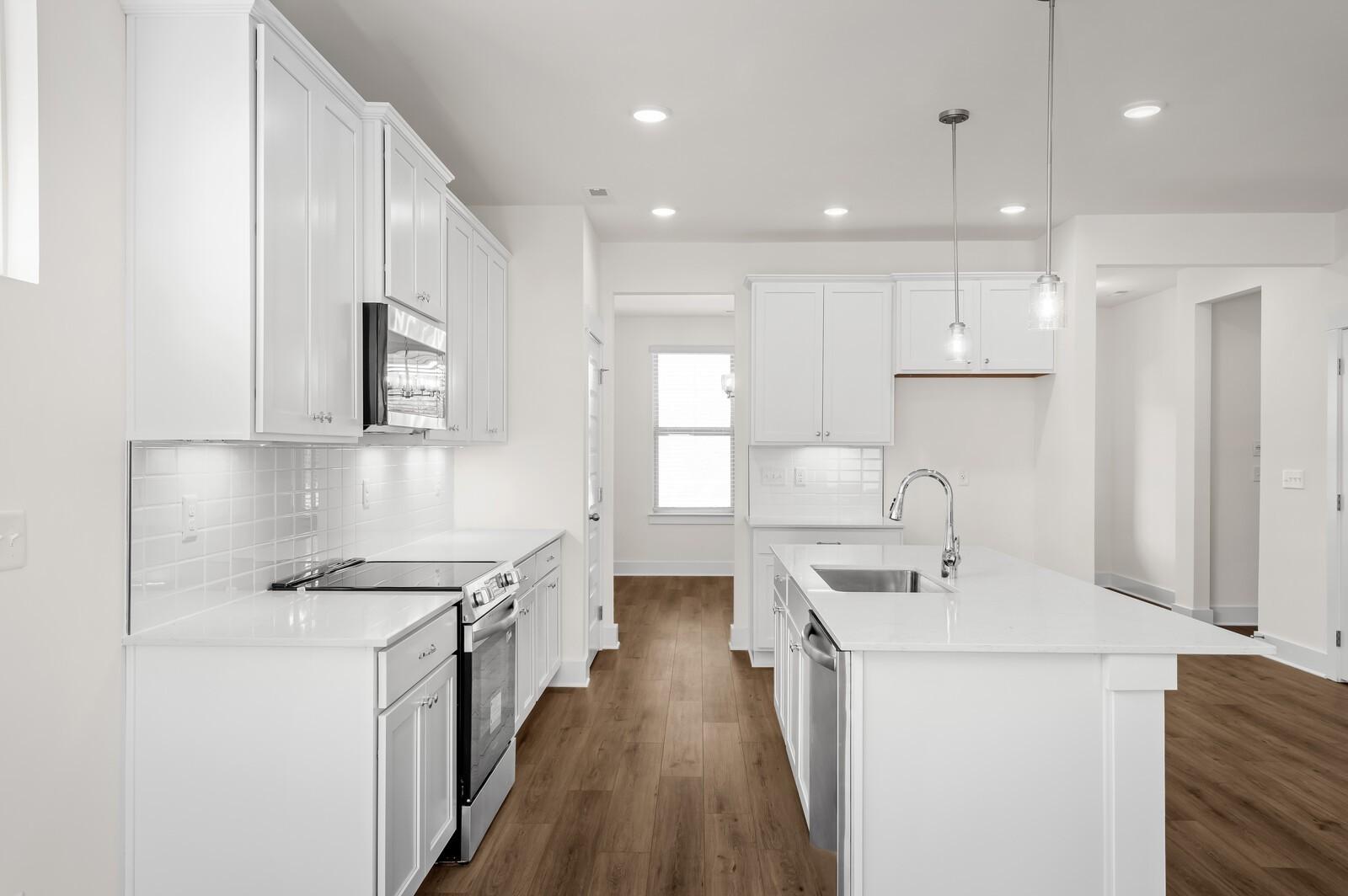 Modern kitchen with white cabinets, quartz countertops, and island in The Ash A floor plan at Woods Crossing, Gallatin, TN.