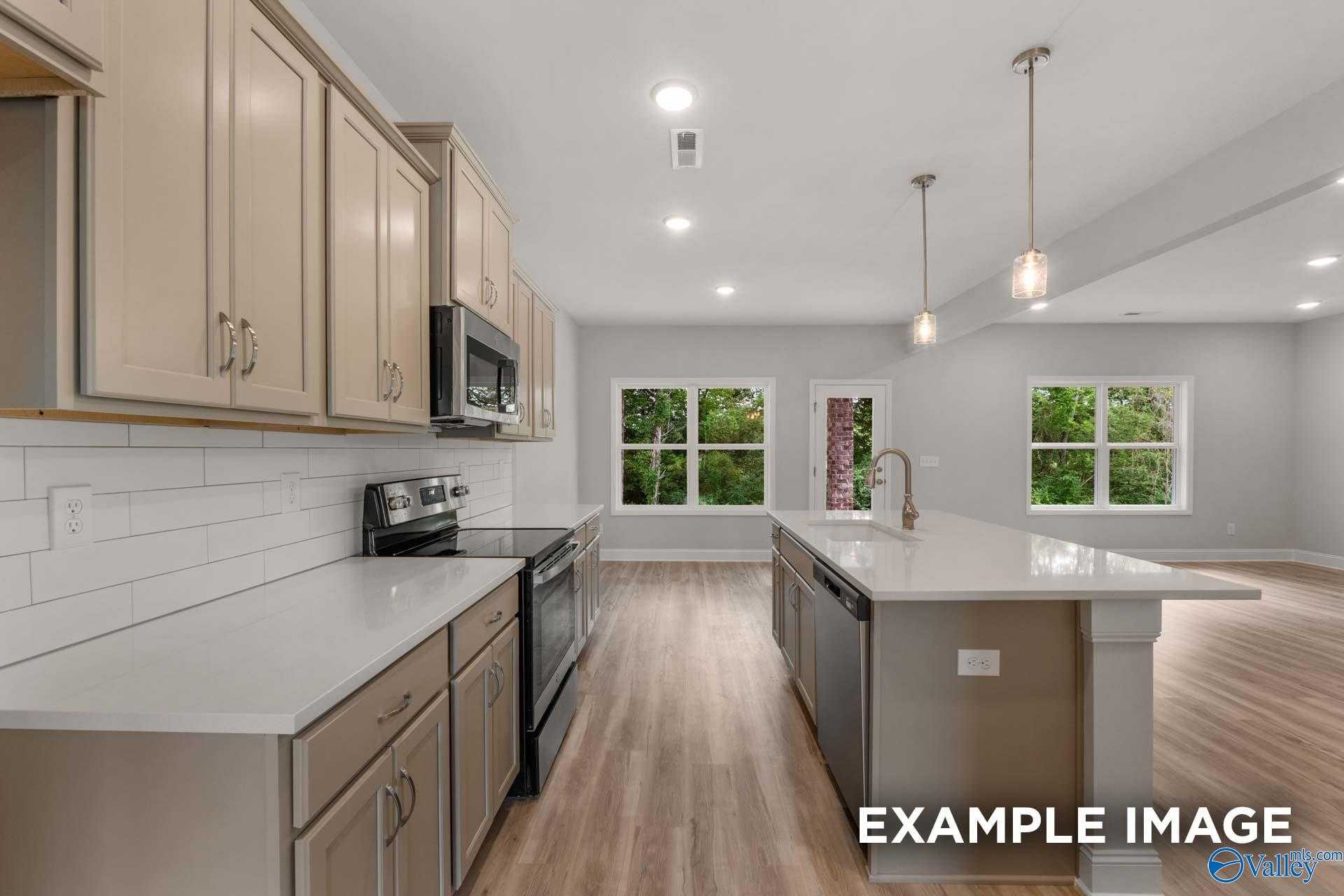 Open-concept kitchen with beige cabinets, quartz island, stainless appliances, and large windows in The Shelby C by Davidson Homes, Meridianville, AL