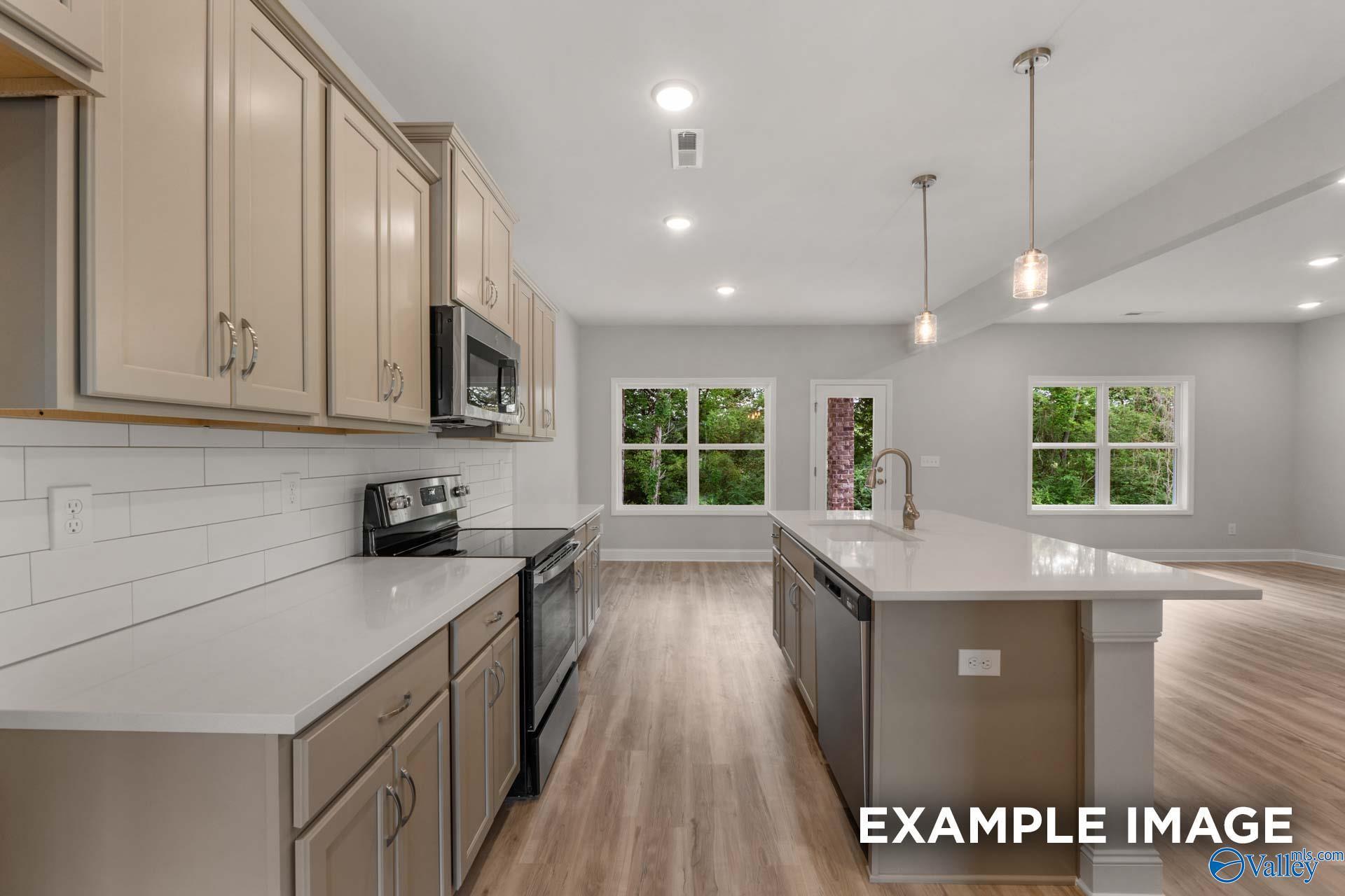 Open-concept kitchen with beige cabinets, quartz island, stainless appliances, and large windows in The Shelby C by Davidson Homes, Meridianville, AL