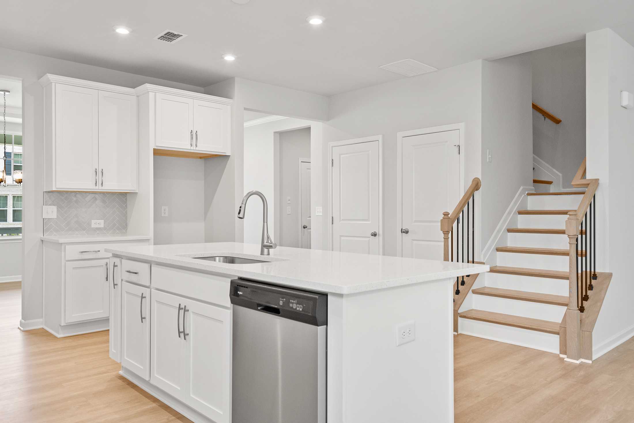 Spacious main-floor kitchen in The Ash B featuring white shaker cabinets, quartz island with sink, and open staircase