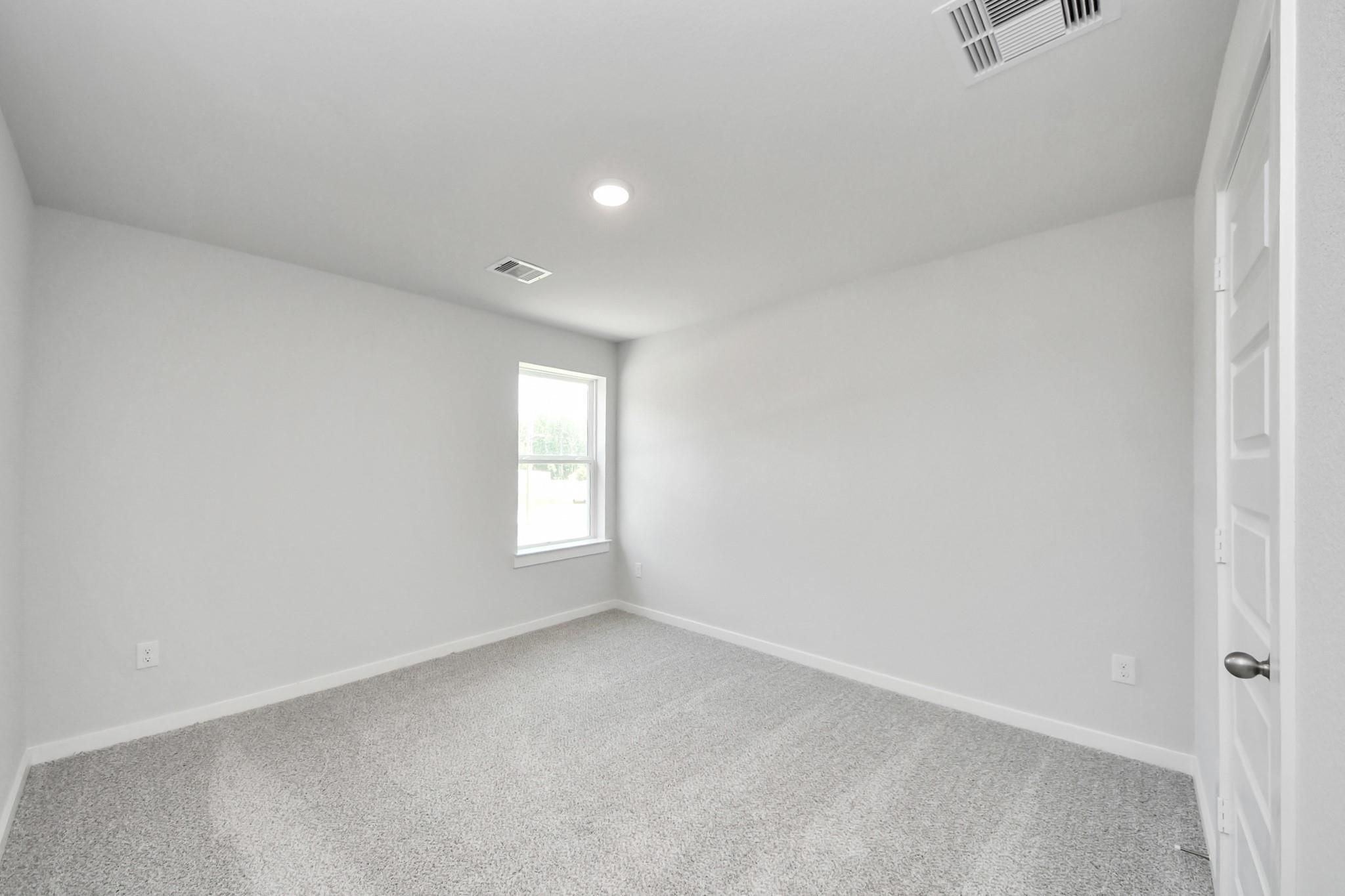 Spacious, carpeted bedroom with neutral walls and natural light in The Sabine F floor plan, Liberty Estates, Cleveland, TX.