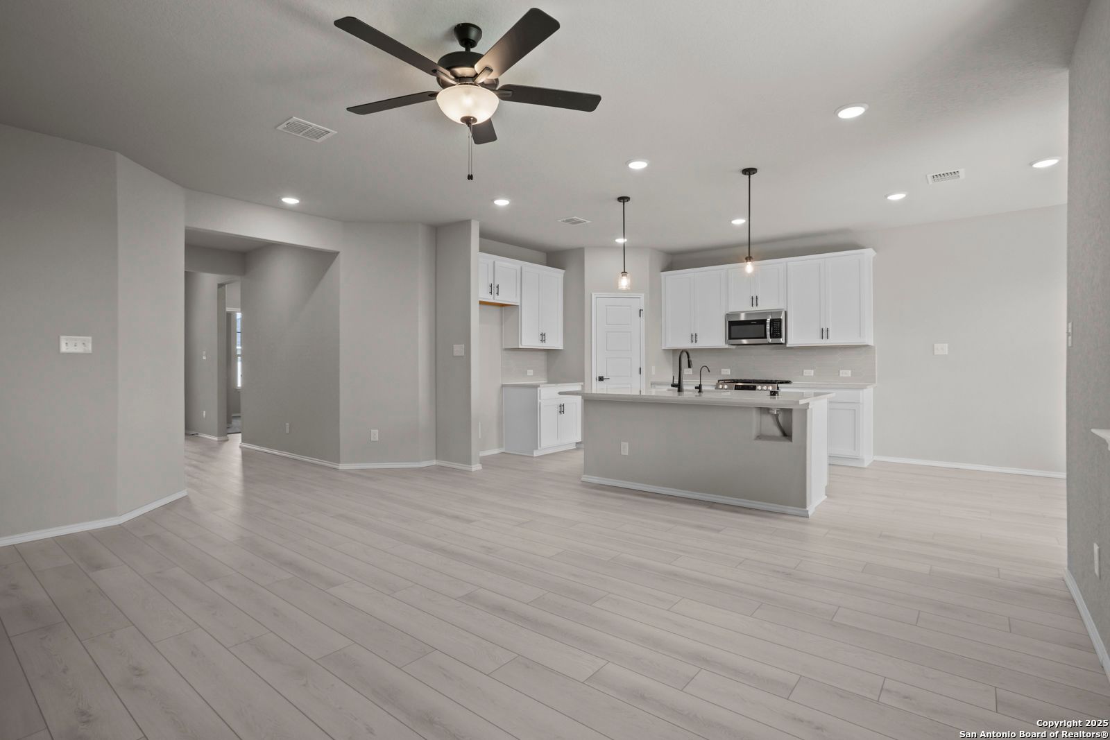 Open-concept kitchen with white shaker cabinets, stainless appliances, large island, and ceiling fans in Davidson Homes The Asheville E, Converse, Texas