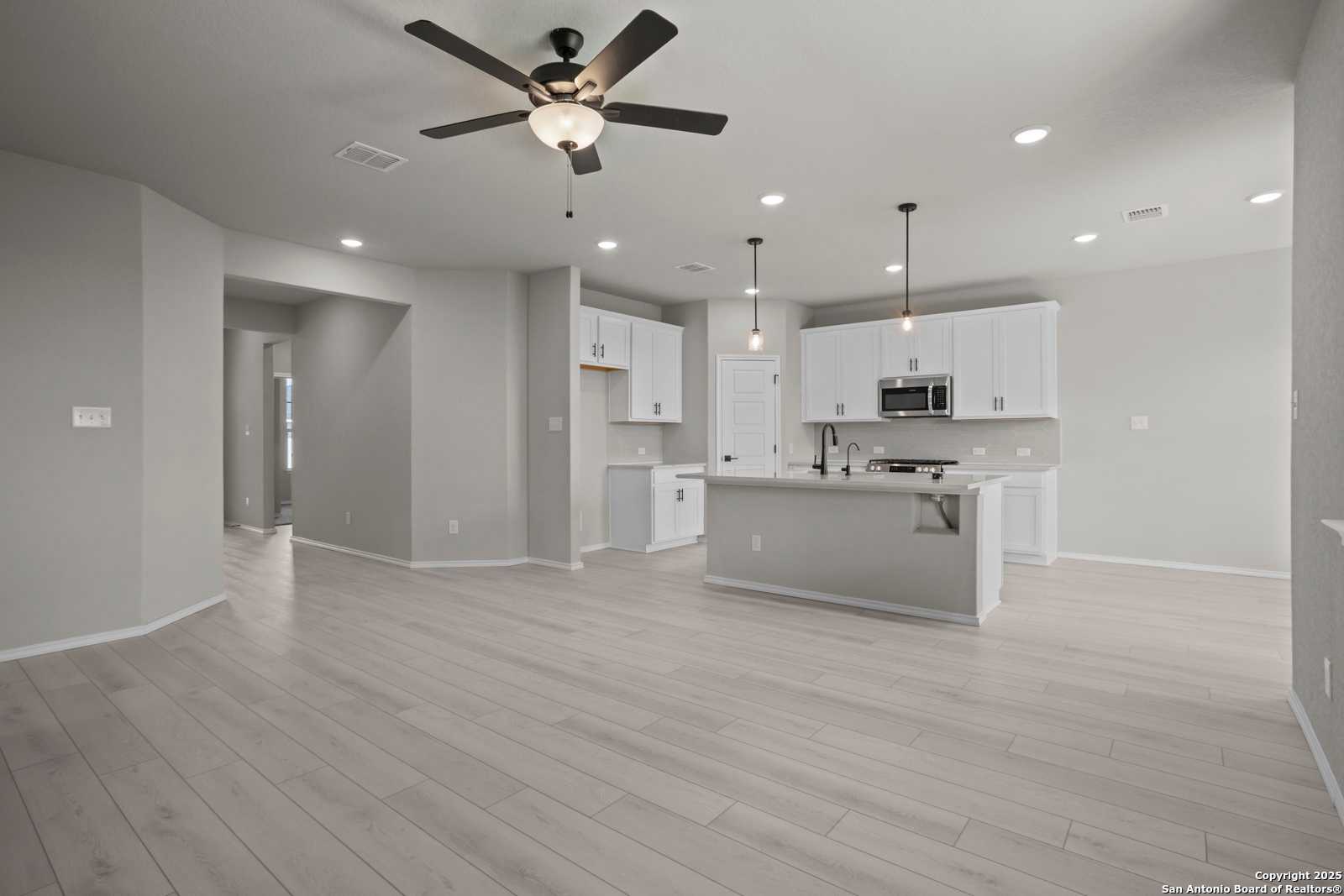 Open-concept kitchen with white shaker cabinets, stainless appliances, large island, and ceiling fans in Davidson Homes The Asheville E, Converse, Texas