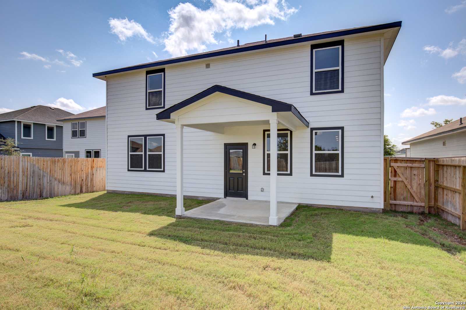 Two-story white home back view with covered patio, black door, large windows, fenced grassy yard in Hannah Heights, Seguin, Texas Davidson Homes Douglas D