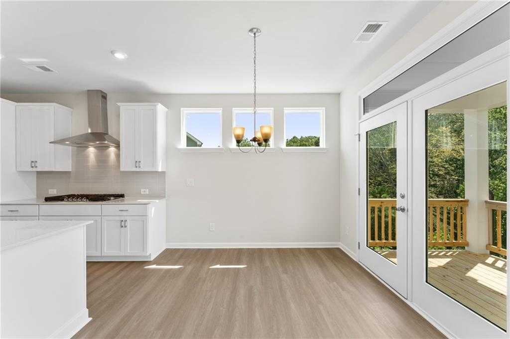 Bright open-concept kitchen with white cabinets, stainless range hood, and French doors to deck in Davidson Homes The Ash B, Riverwood, Dallas, GA