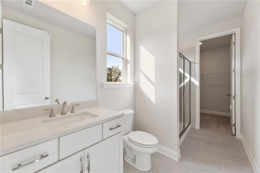 Bright bathroom with white vanity, single sink, glass shower, toilet, and window in The Hampton C by Davidson Homes, Buford, GA
